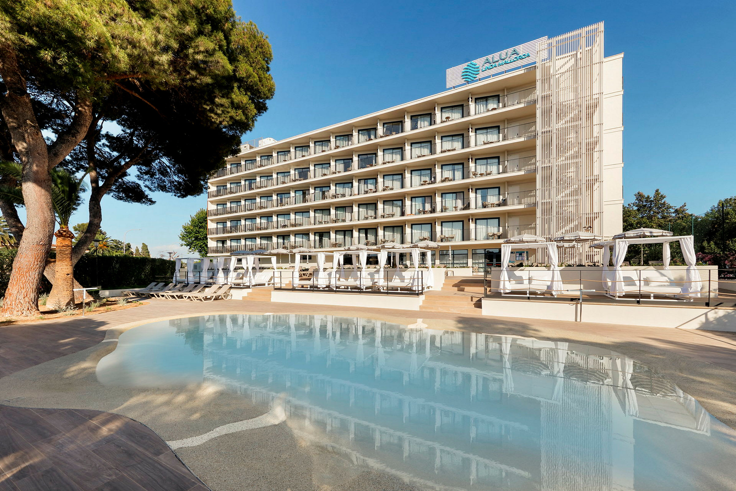Et hotel set fra poolområdet med liggestole og cabanas. (AI-genereret tekst)