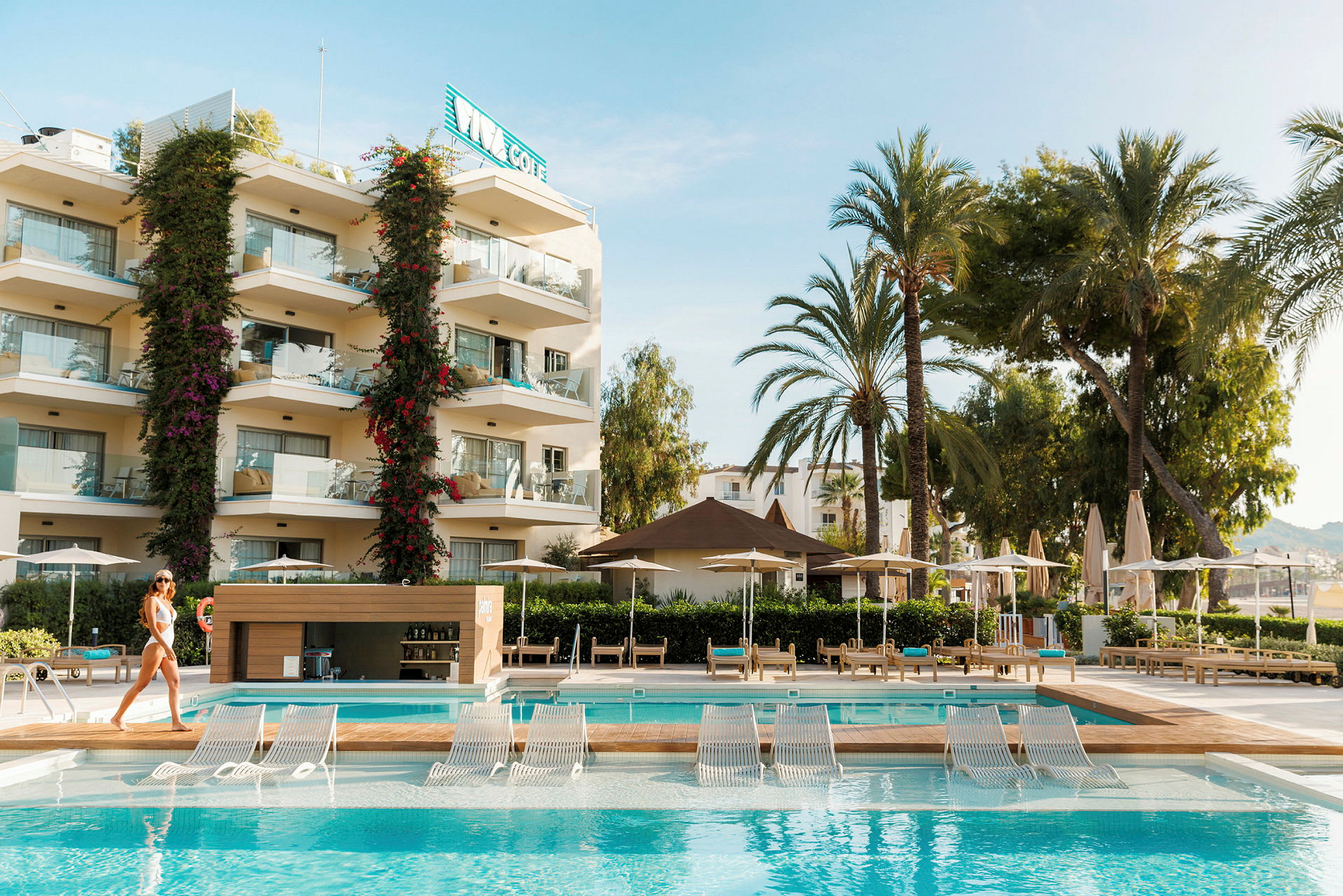 Hotelområde med pool og liggestole, omgivet af palmer. (AI-genereret tekst)