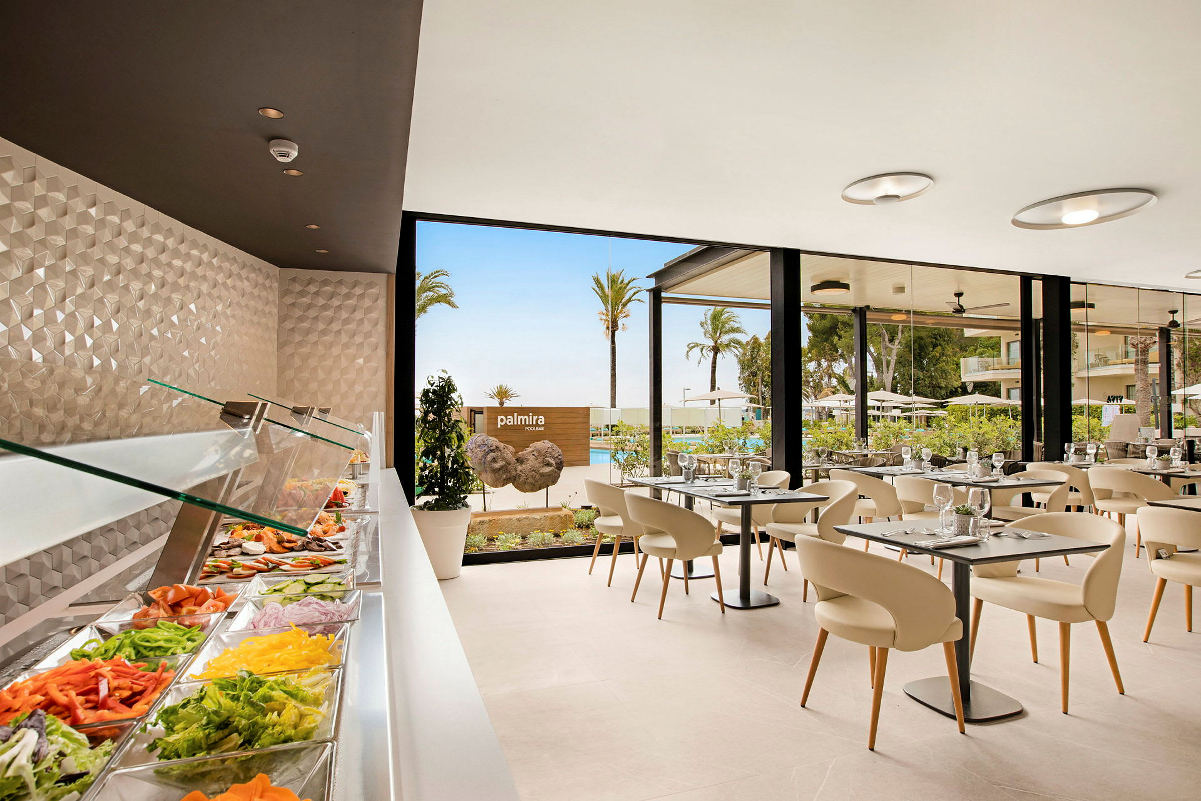 Buffet med grøntsager i et glasindrammet serveringsområde, spisested med borde og stole ved vinduer med udsigt over palmer og pool. (AI-genereret tekst)