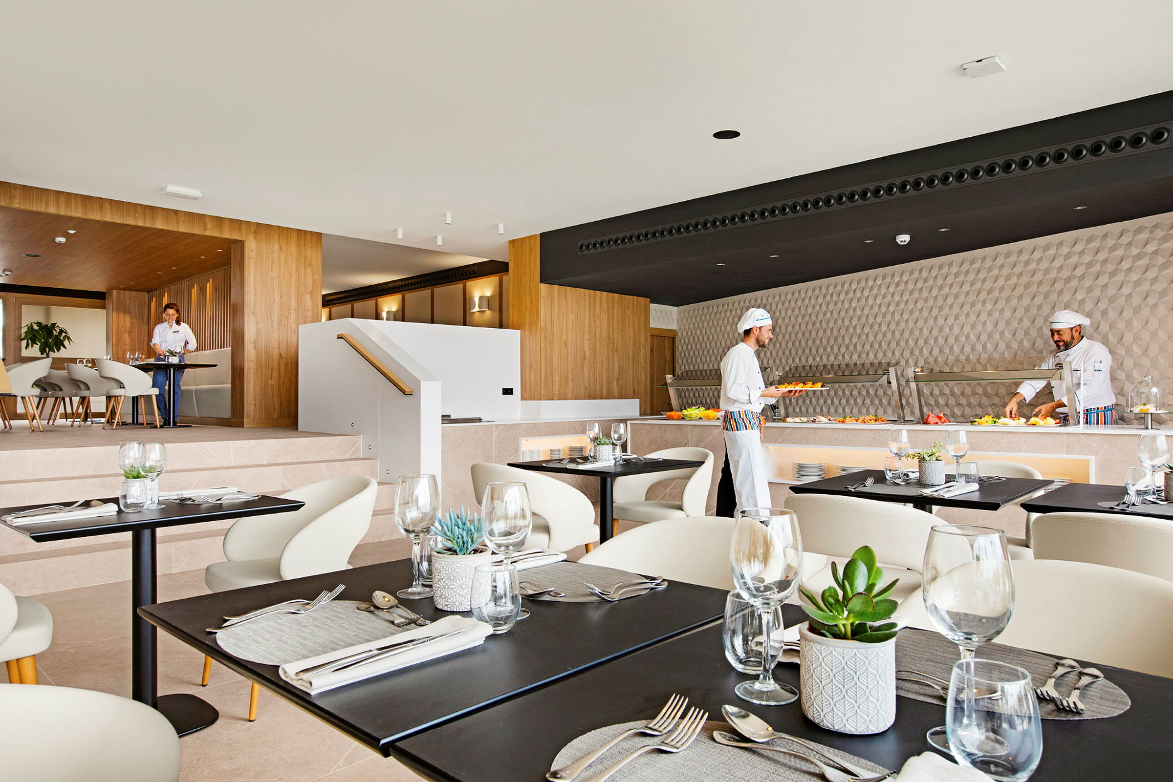 En moderne restaurantindretning med dækkede borde. Kokke forbereder mad ved en buffet. (AI-genereret tekst)
