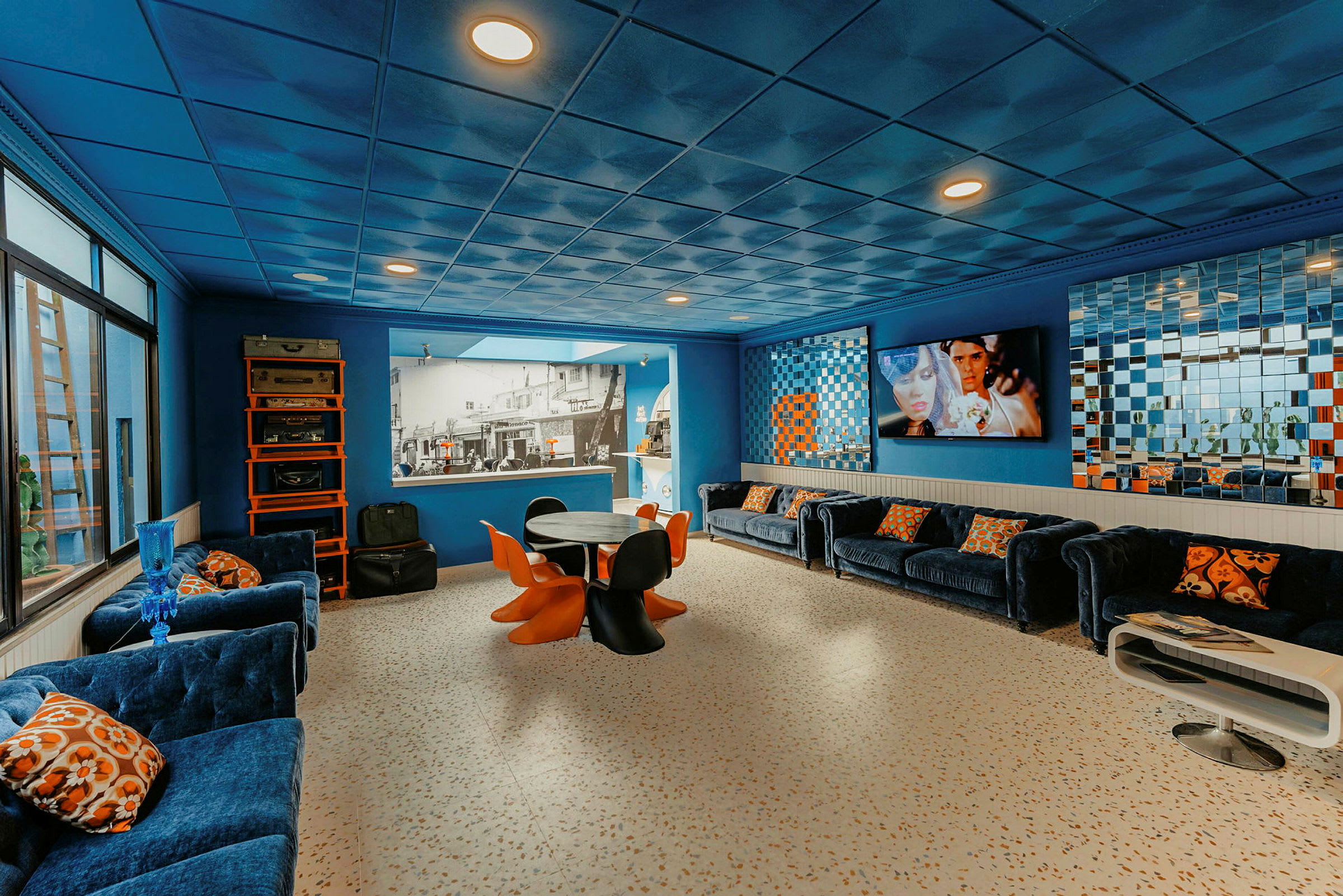 Et rum med blå indretning, sofaer, et bord med orange stole og spejlvægge. (AI-genereret tekst)