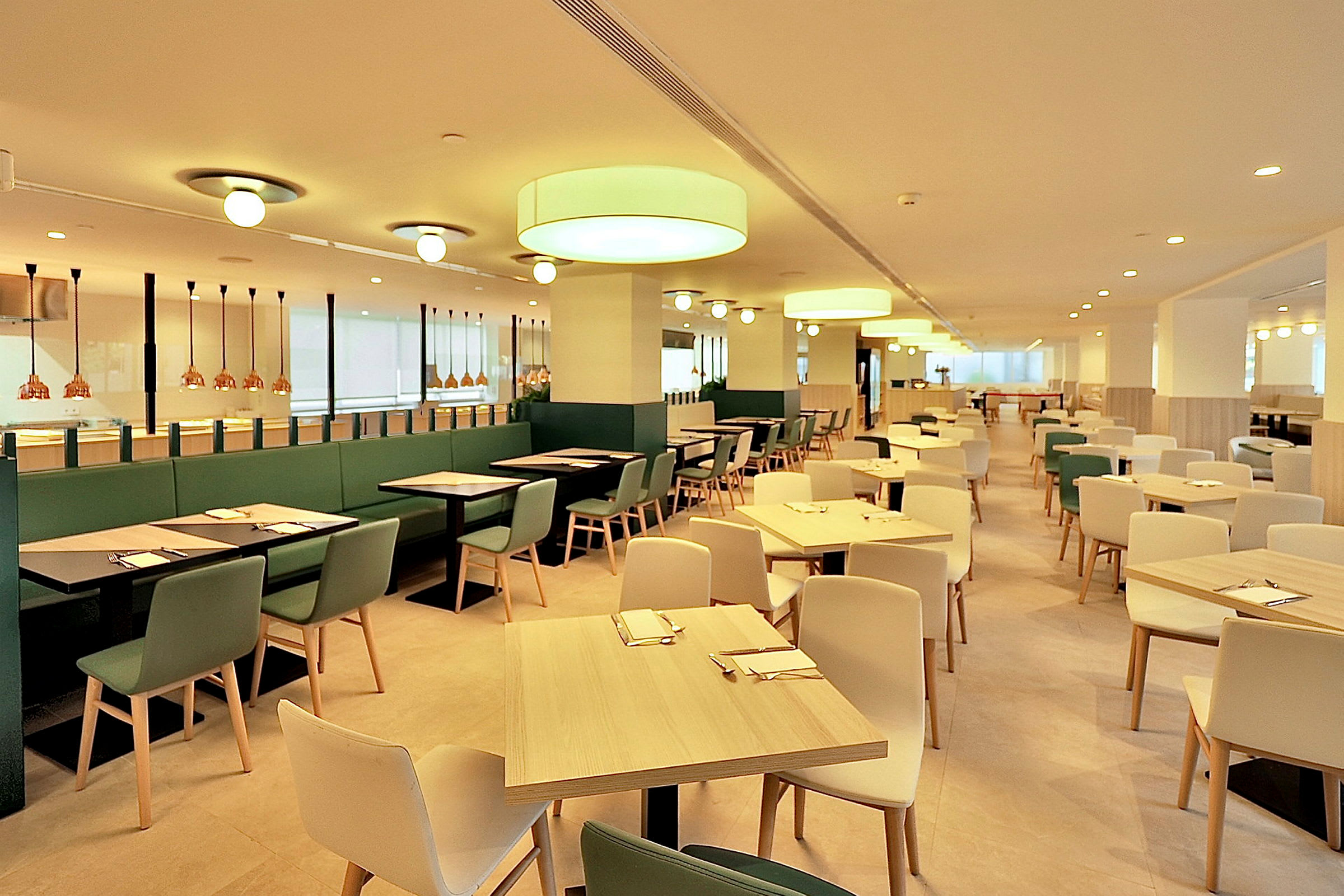 En lys og rummelig restaurant med moderne møbler og belysning. Borde og stole er arrangeret i jævne rækker. (AI-genereret tekst)