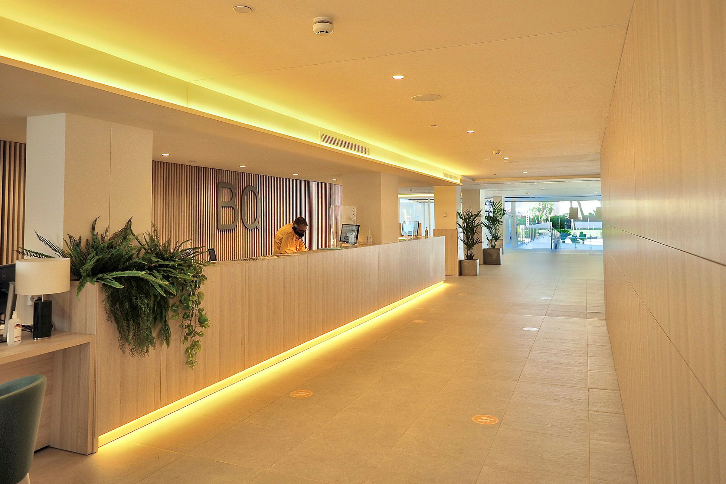 Lyset hotellets reception med en langt træskranke, moderne detaljer og plantepynt. (AI-genereret tekst)
