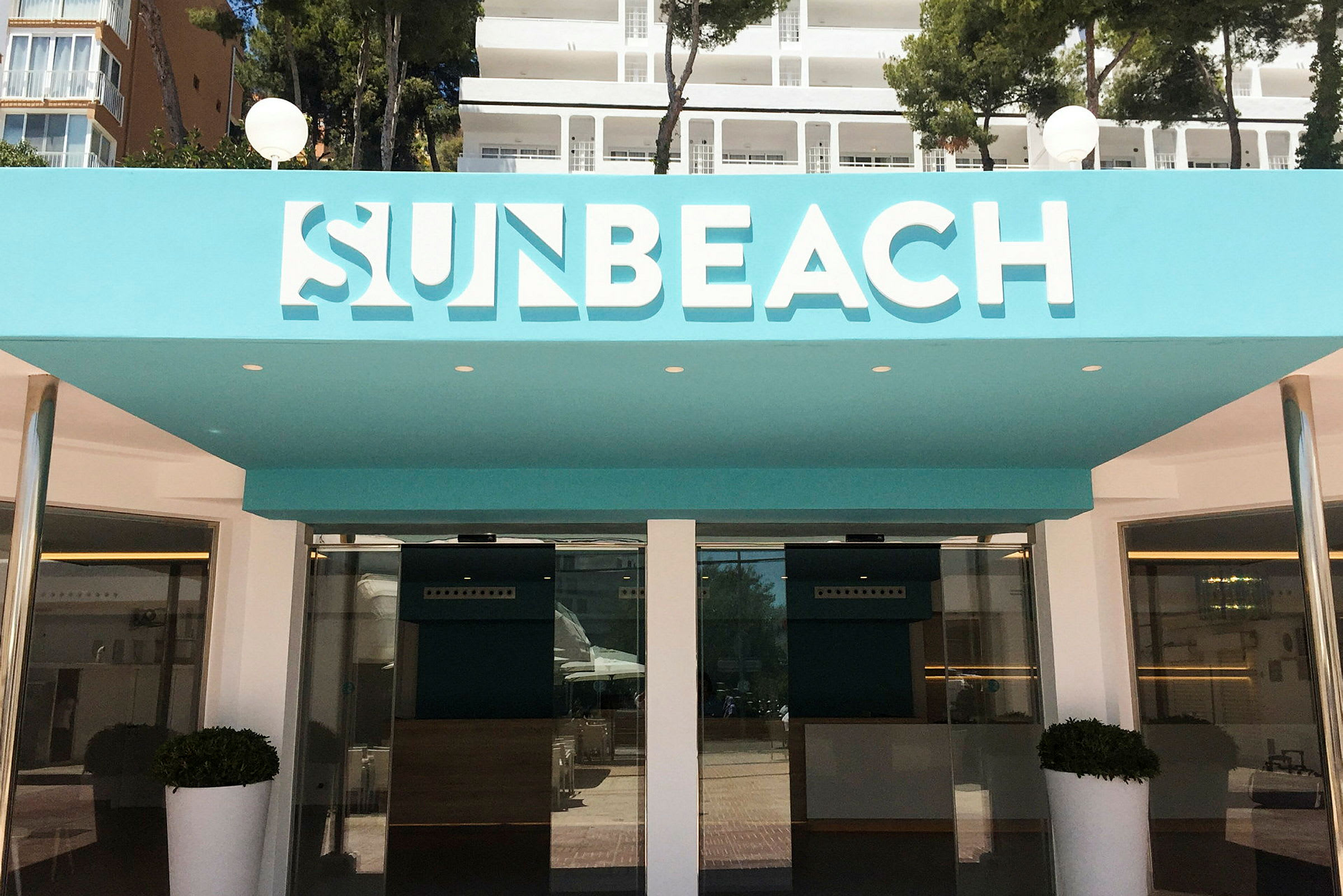 Indgangen til Sun Beach-hotellet med turkis detaljer. (AI-genereret tekst)