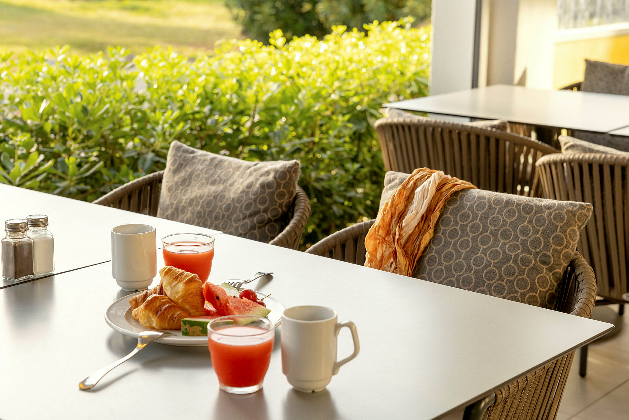 Morgenmad med croissanter, vandmelon og juice på et bord med havemøbler. (AI-genereret tekst)