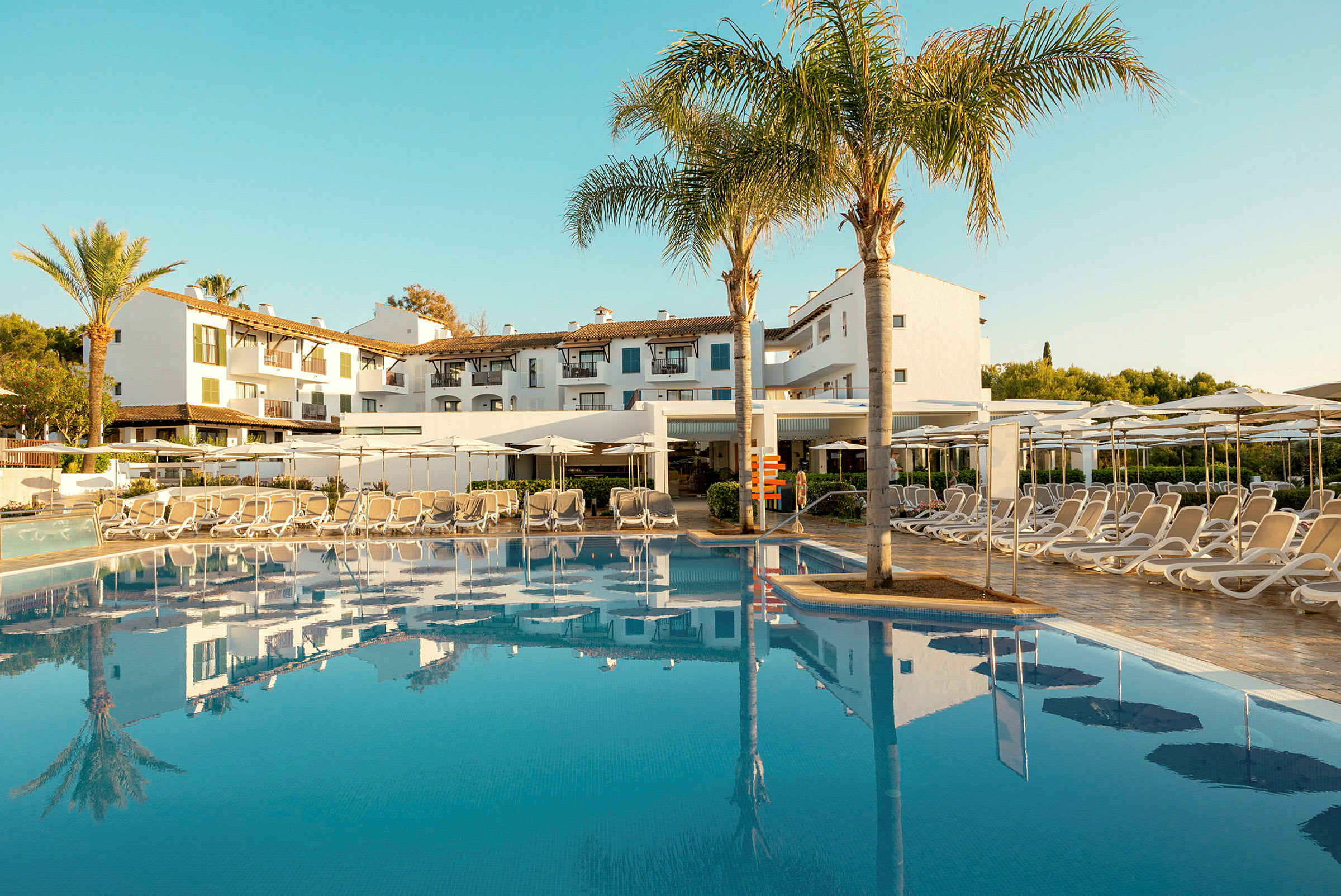 Hotelbygning bag en pool med solsenge og parasoller. (AI-genereret tekst)