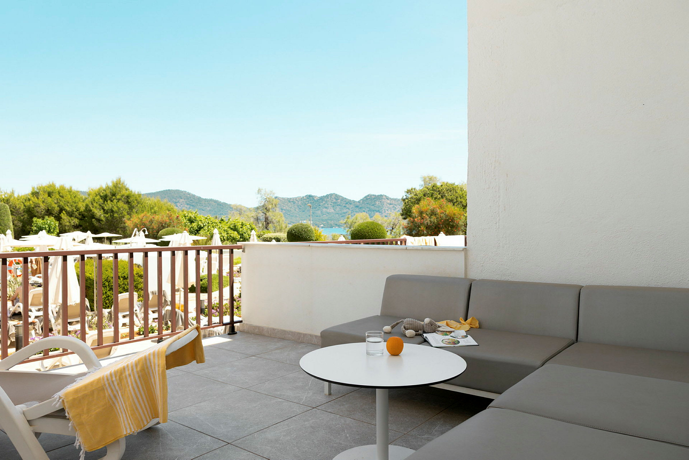 Terrasse med grå sofa, hvidt bord og udsigt over have og bjerge. (AI-genereret tekst)