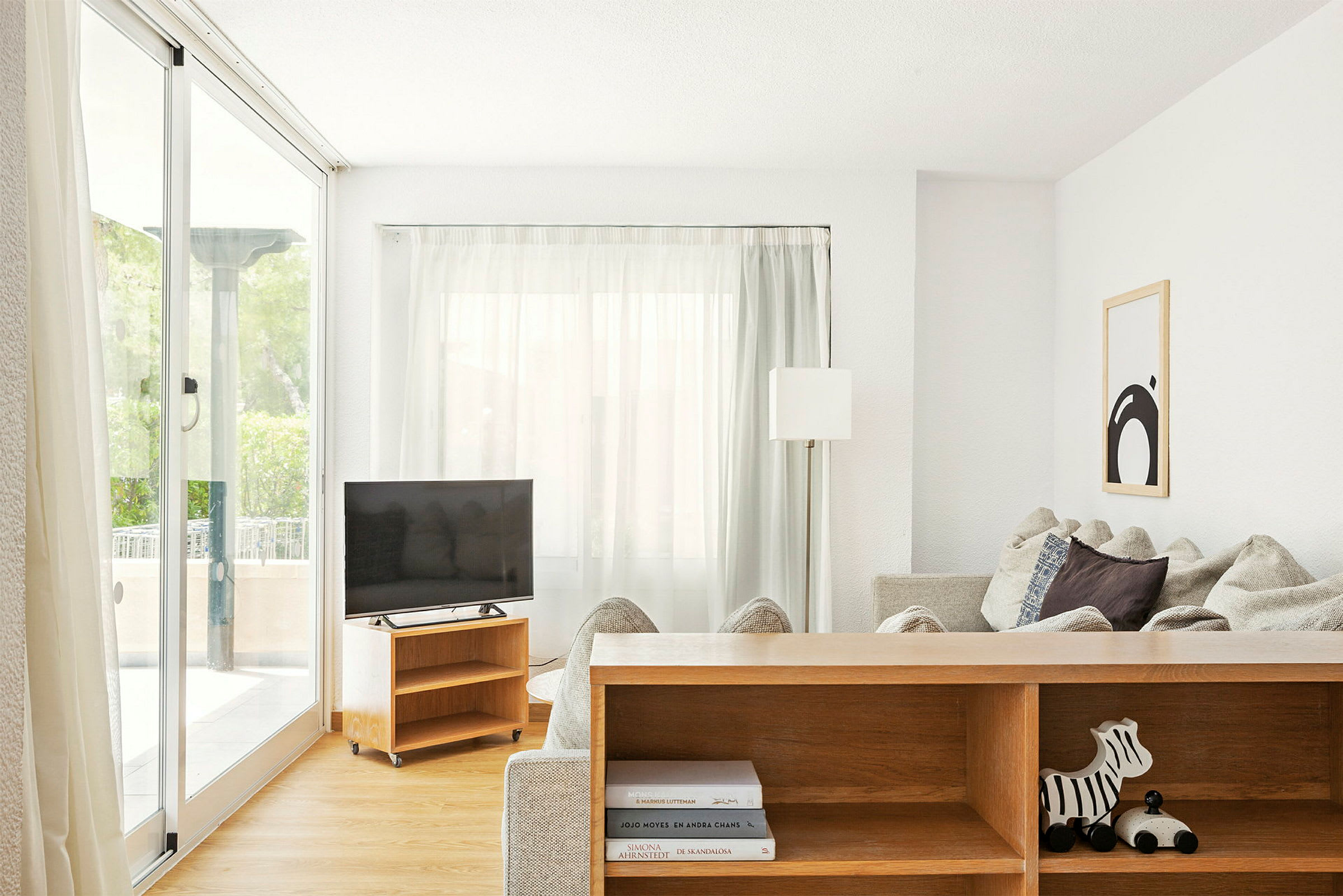 Stue med store vinduer, sofa, tv og en bogreol. (AI-genereret tekst)