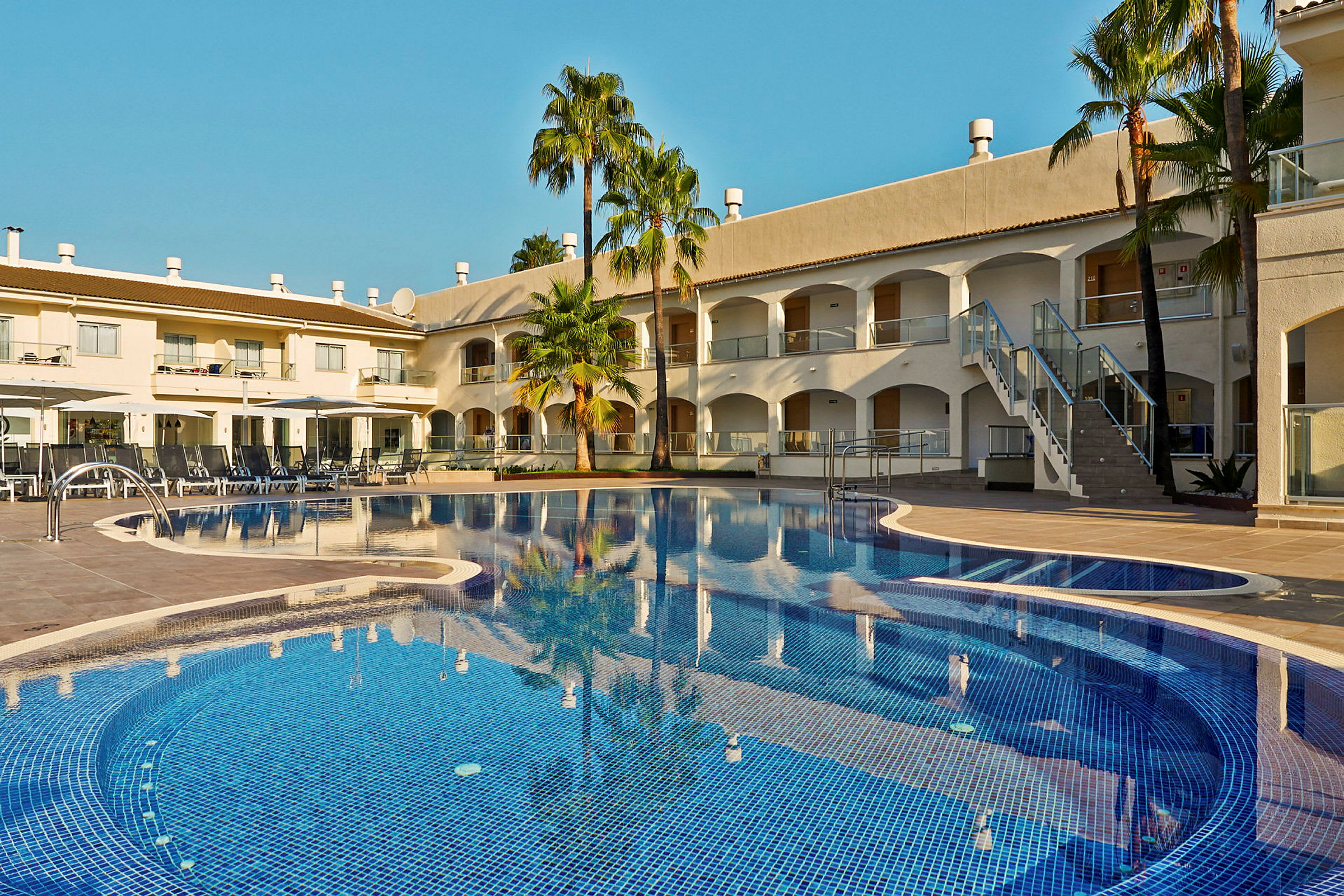 Billede af en hotelpool med liggestole og bygninger i baggrunden. (AI-genereret tekst)