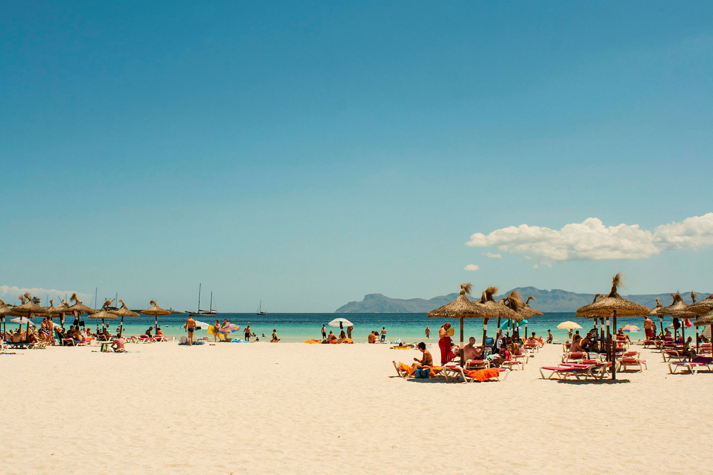 Strand med parasoller og liggestole, folk bader og nyder solen. (AI-genereret tekst)