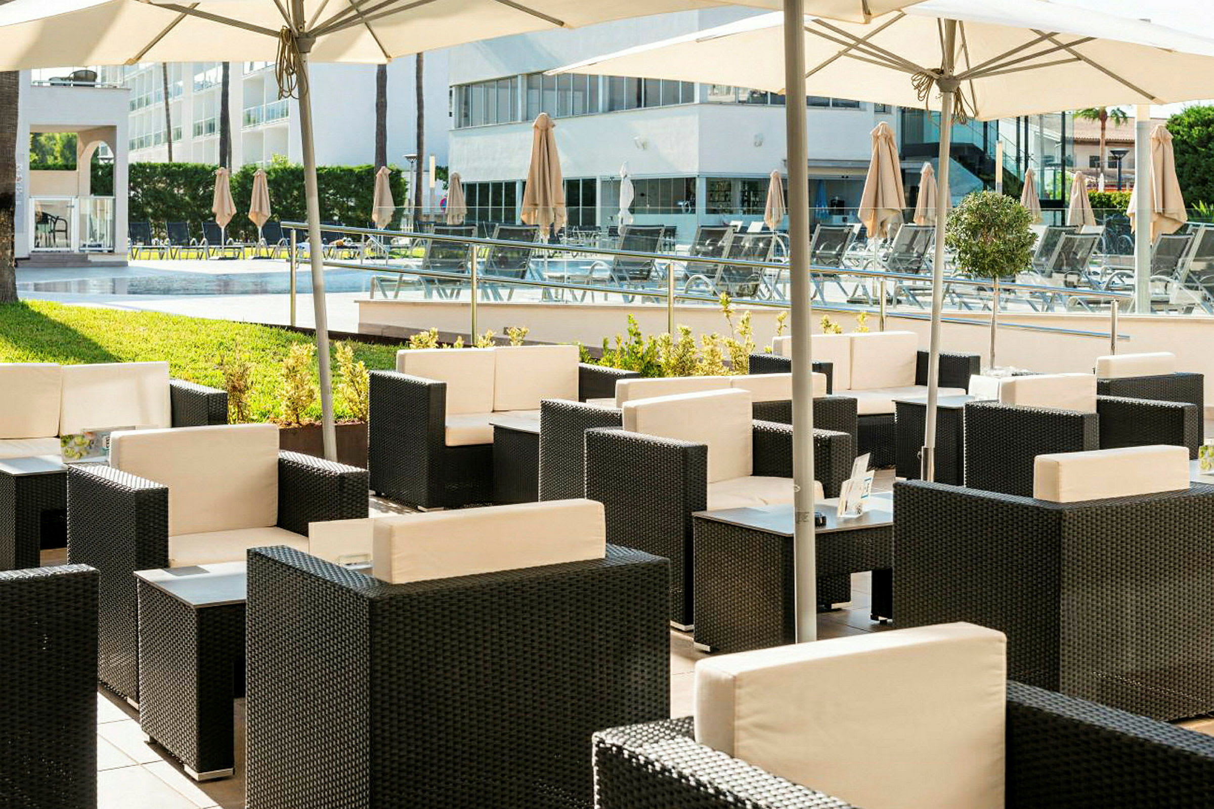 En udendørs terrasse med flettede møbler og parasoller ved en pool. (AI-genereret tekst)