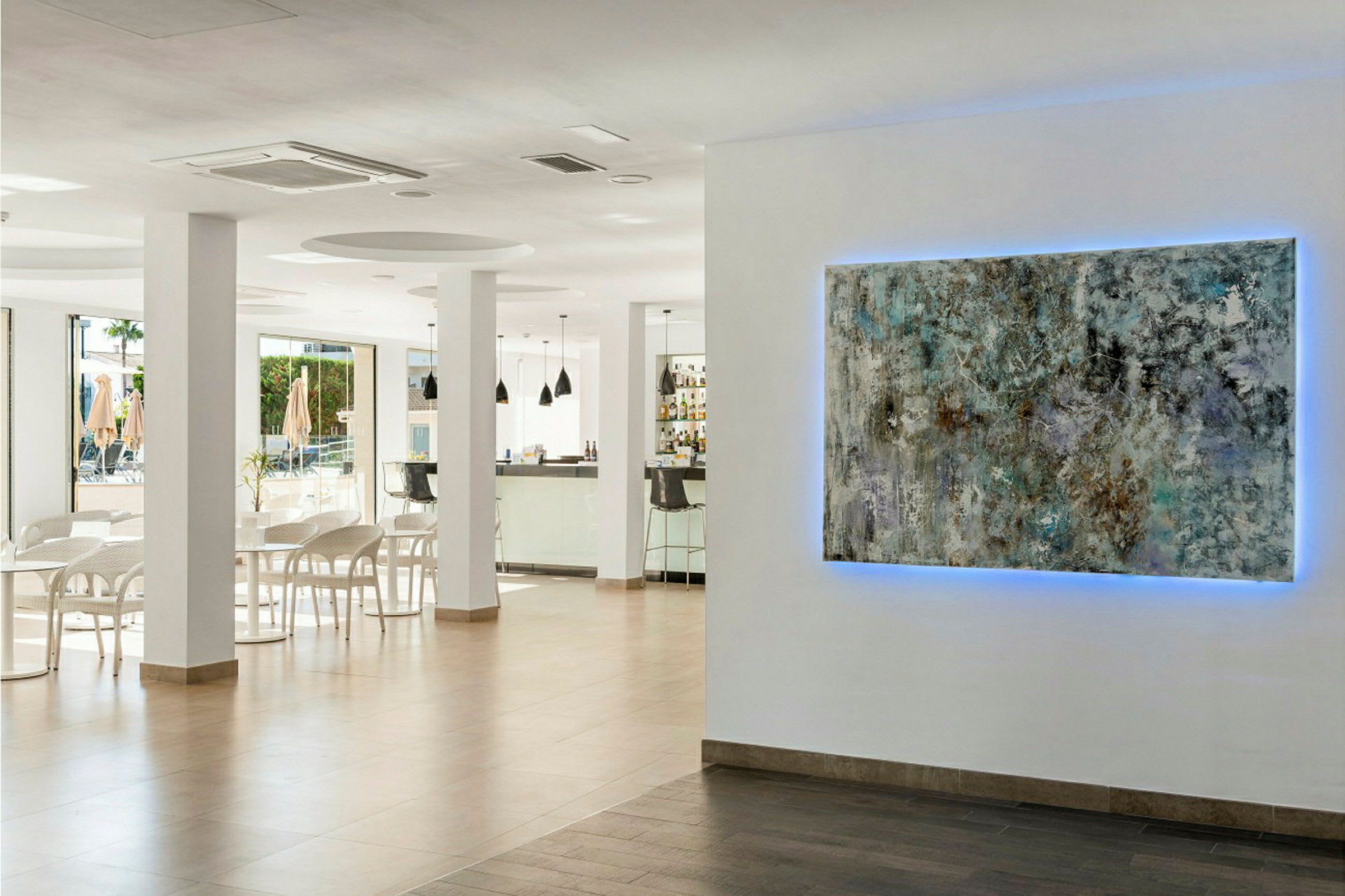 Interiør fra et moderne caféområde. På væggen hænger et kunstværk med blåt lys bagved. (AI-genereret tekst)