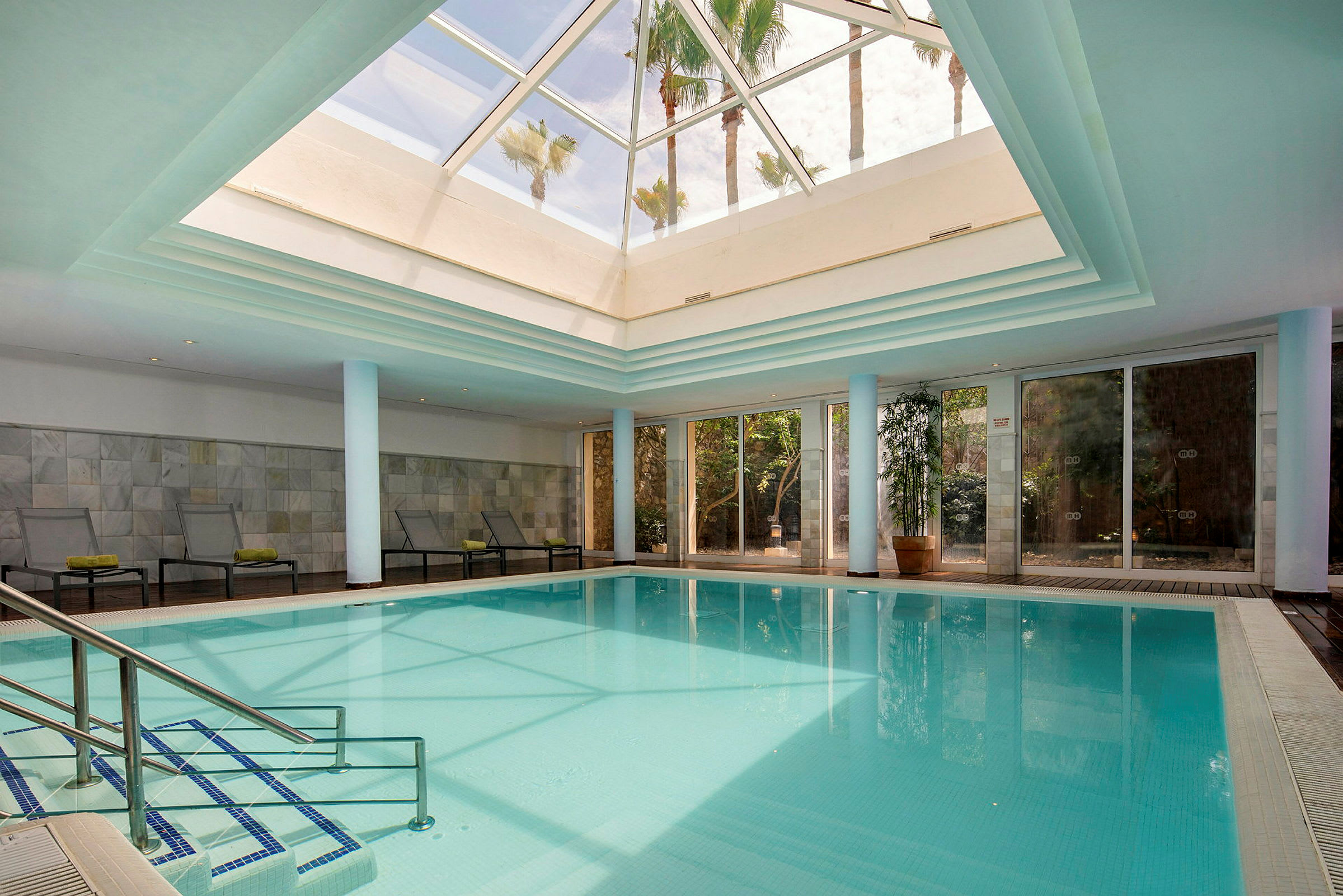 Indendørs pool med glastag og solsenge ved kanten. (AI-genereret tekst)