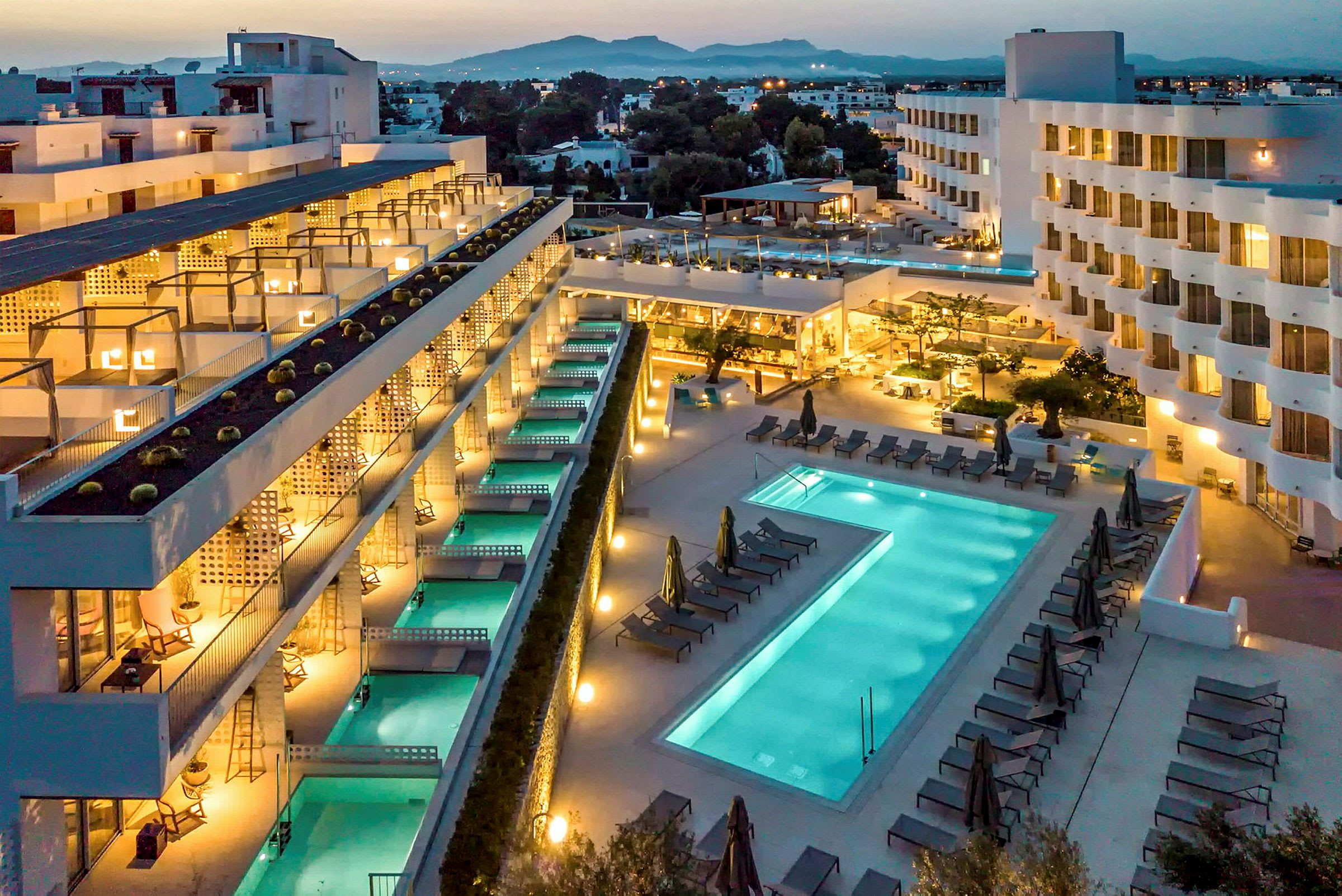 Hotelområde med bygninger, pools og solsenge om aftenen. (AI-genereret tekst)