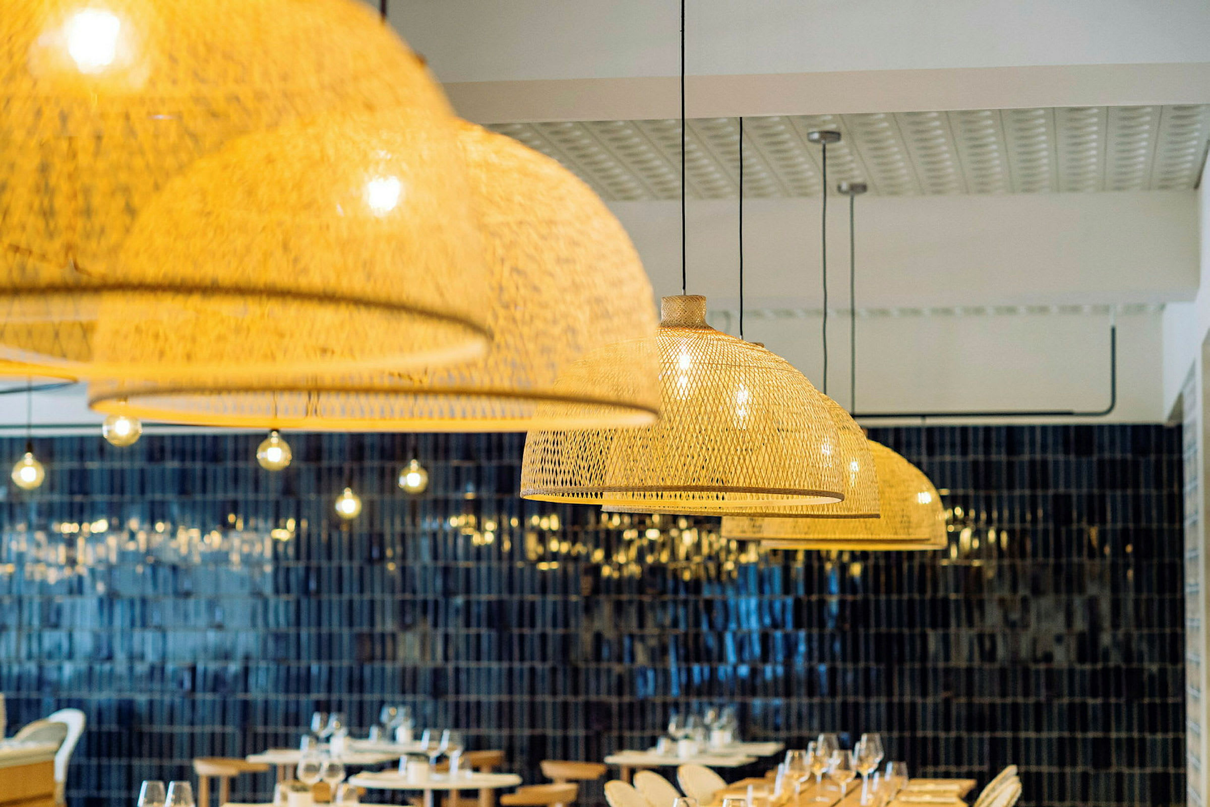 Restaurantinteriør med hængende flettede lampeskærme og borde med opdækning. (AI-genereret tekst)