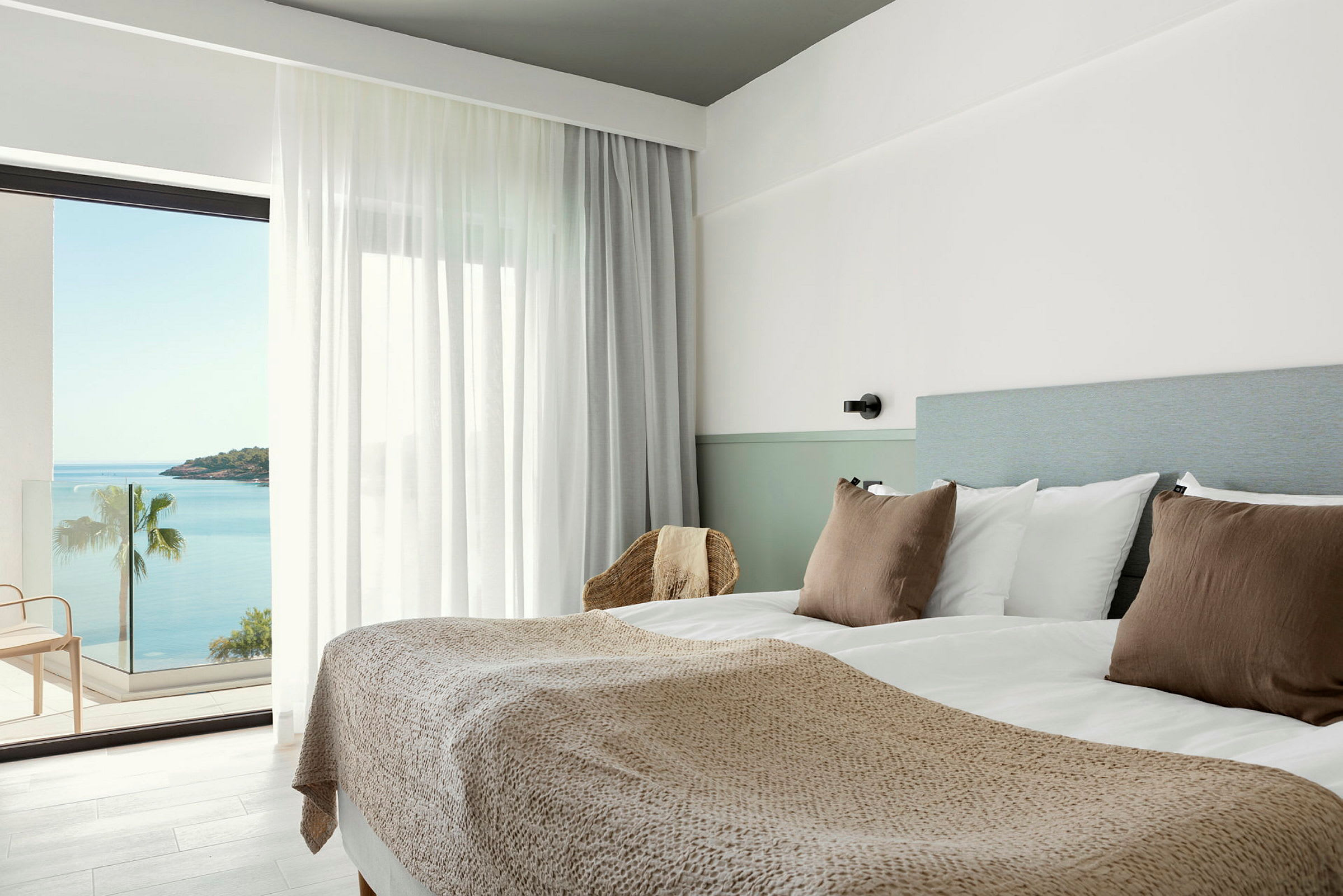 Hotelværelse med dobbeltseng, lyse farver og havudsigt fra altanen. (AI-genereret tekst)