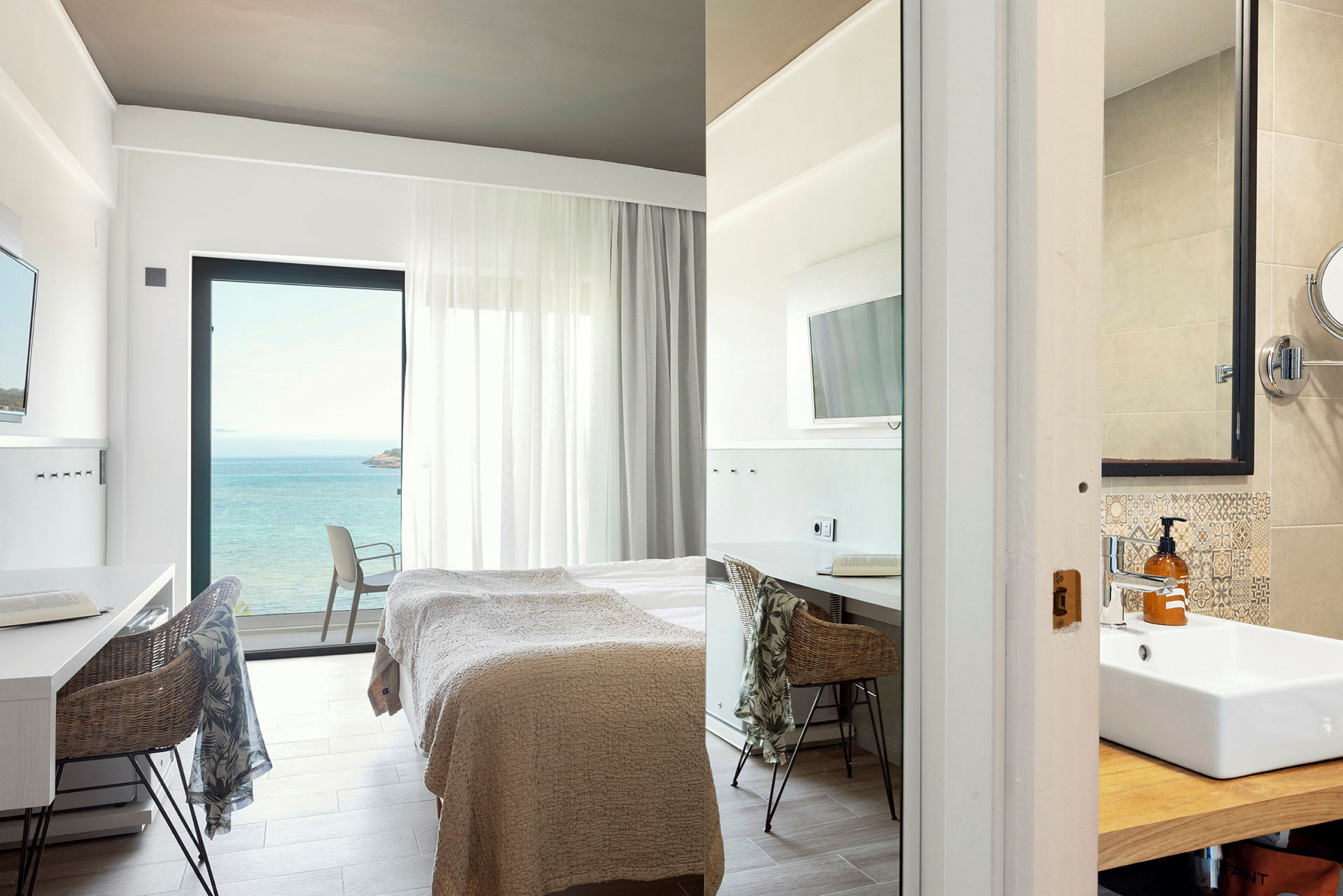 Moderne hotelværelse med havudsigt, seng og arbejdsområde samt del af badeværelse. (AI-genereret tekst)