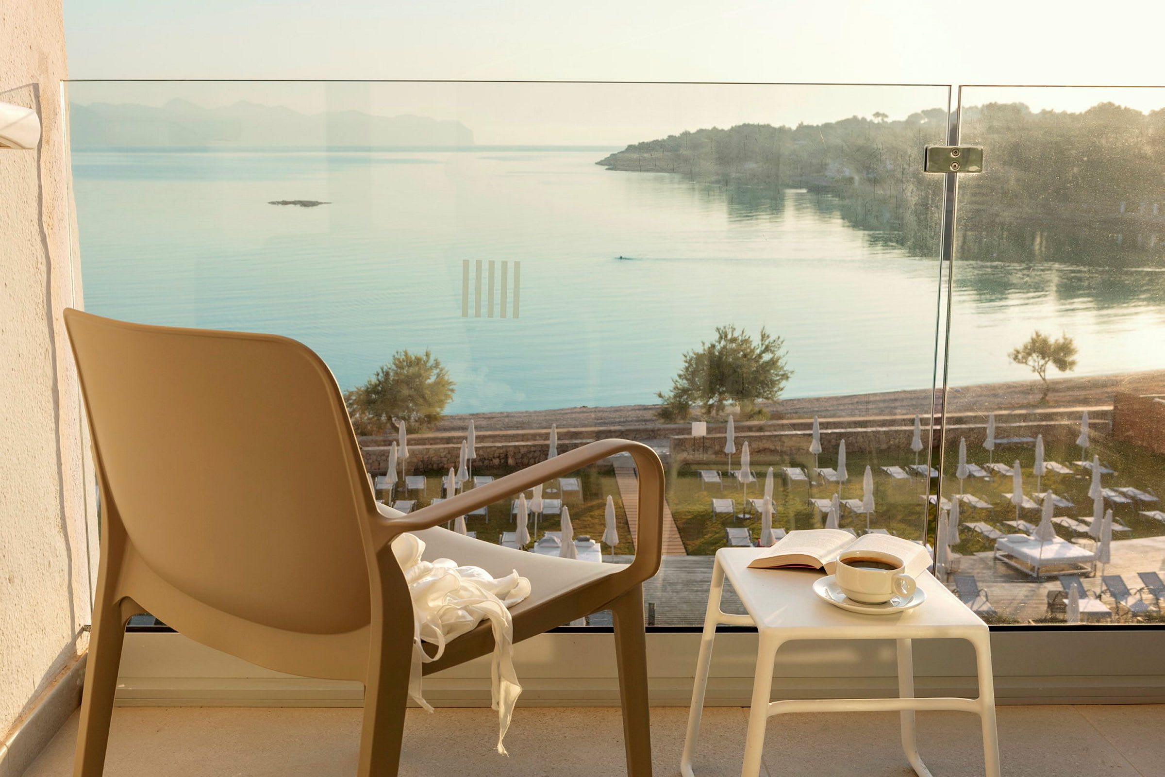 Stol og bord med en kop kaffe og en bog på en terrasse med udsigt over havet. (AI-genereret tekst)