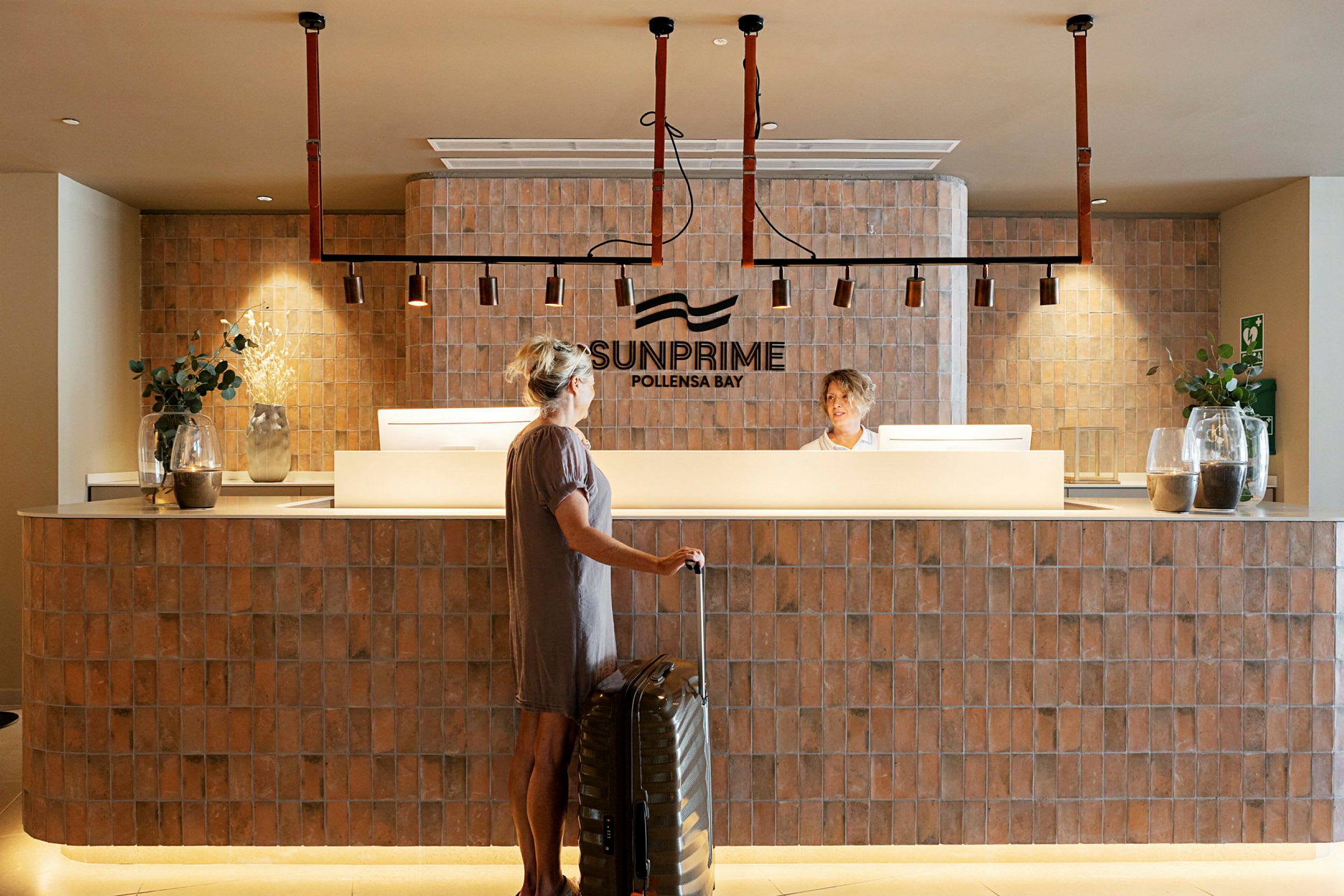 Receptionen på Sunprime Pollensa Bay med en person, der står foran skranken og en kuffert. (AI-genereret tekst)
