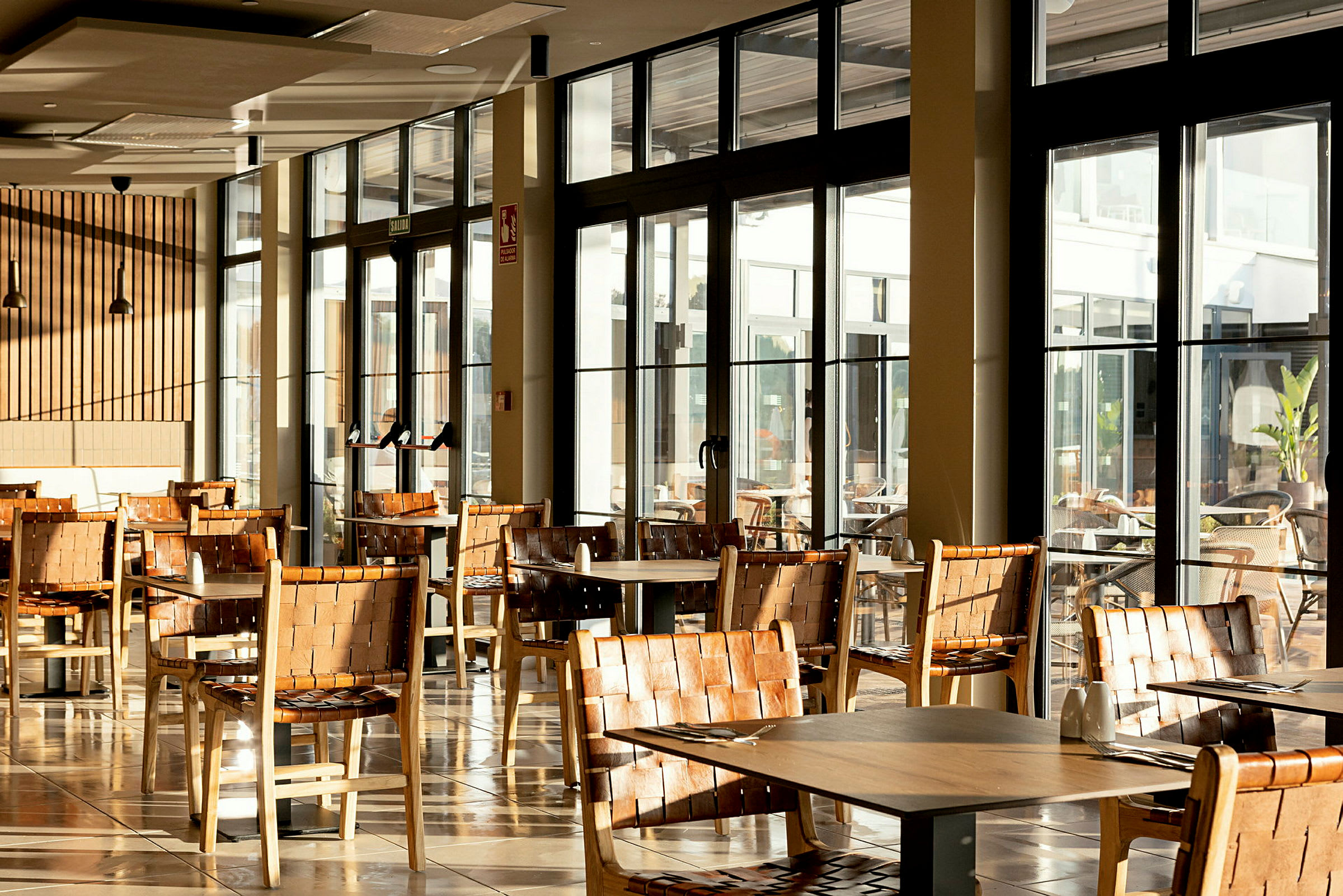 Restaurantområde med borde og træstole, store vinduer med udsigt. (AI-genereret tekst)