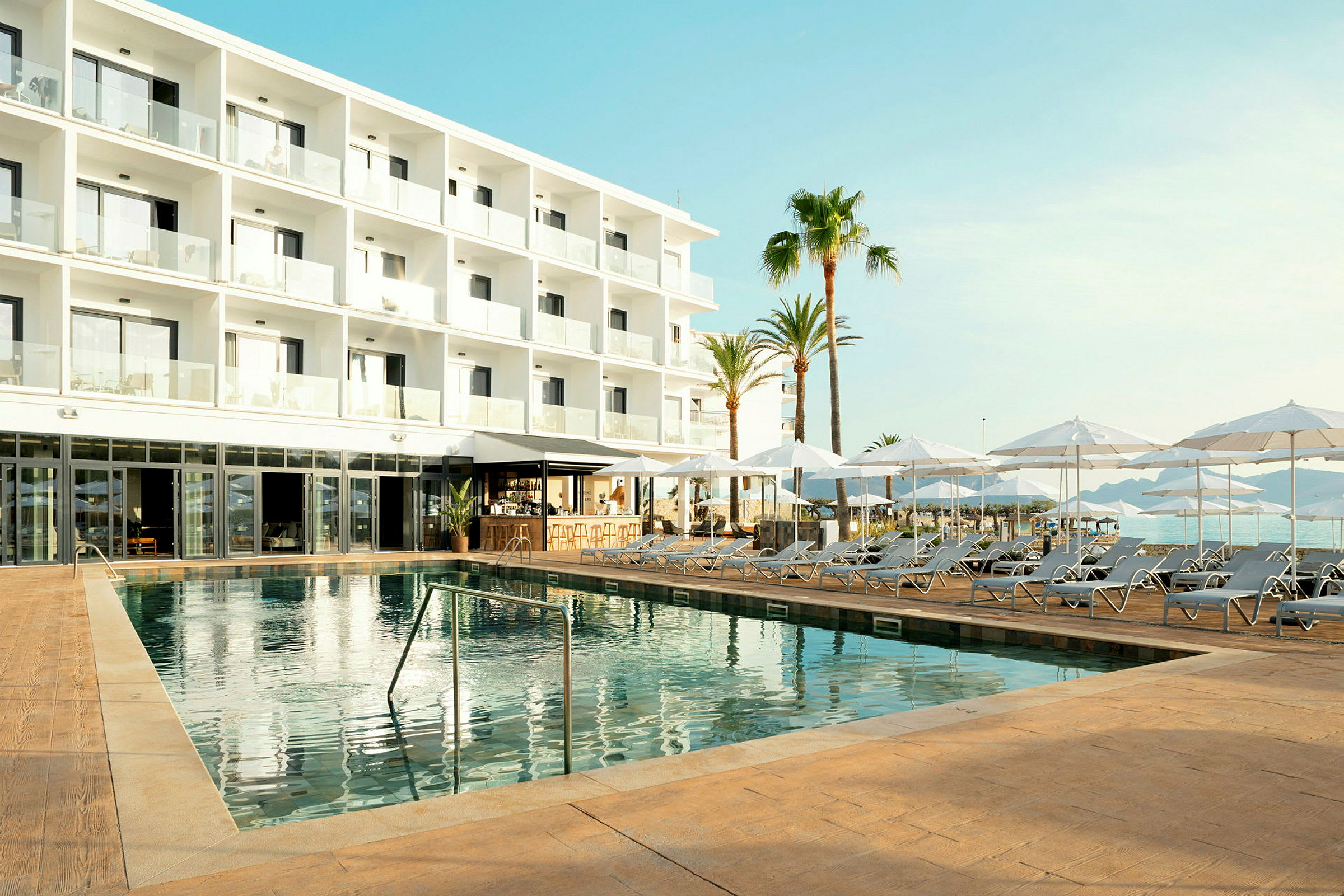 Moderne hotelbygning med områder til liggestole og parasoller samt en swimmingpool. (AI-genereret tekst)