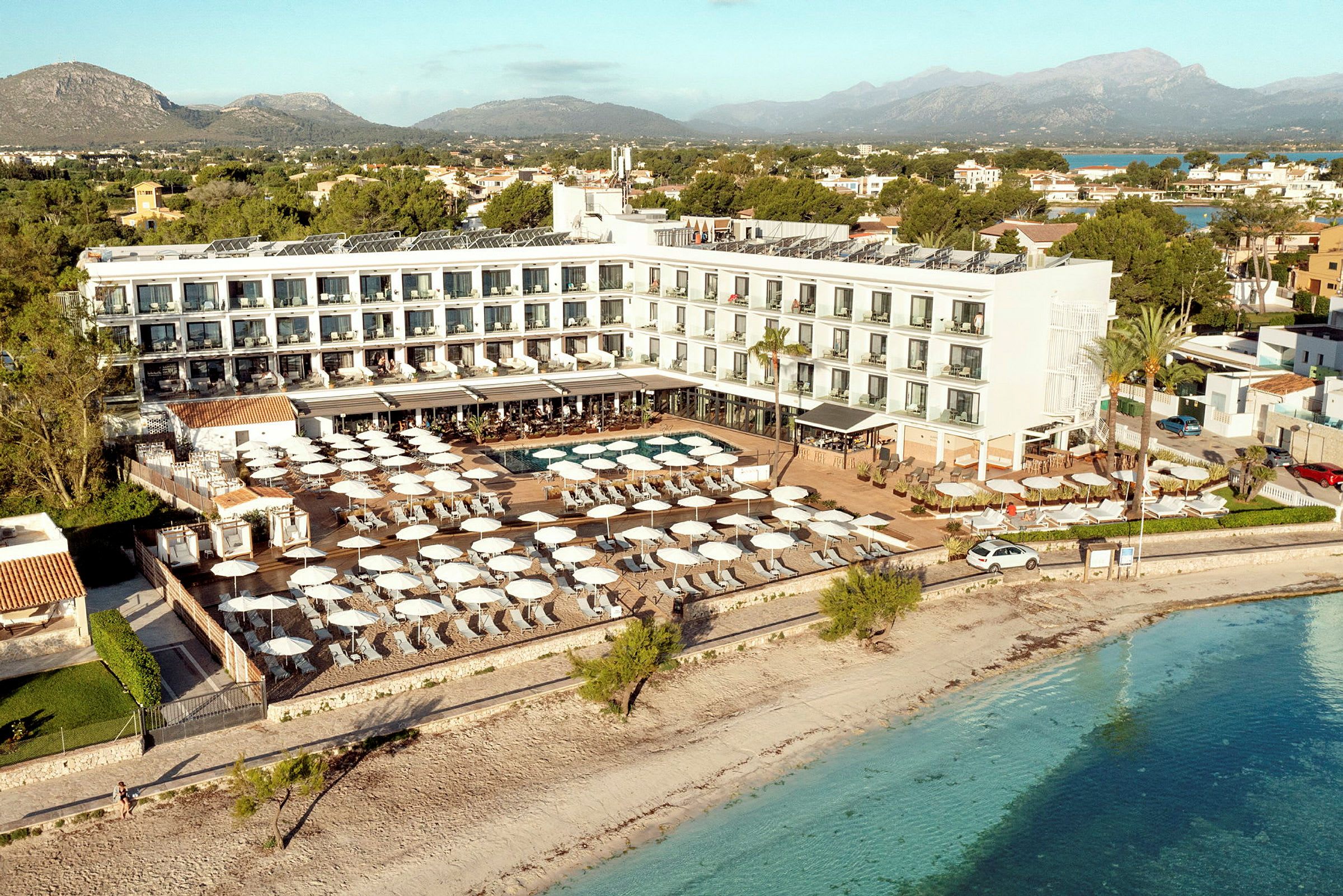 Luftfoto af et hotel ved stranden med poolområde og parasoller. (AI-genereret tekst)