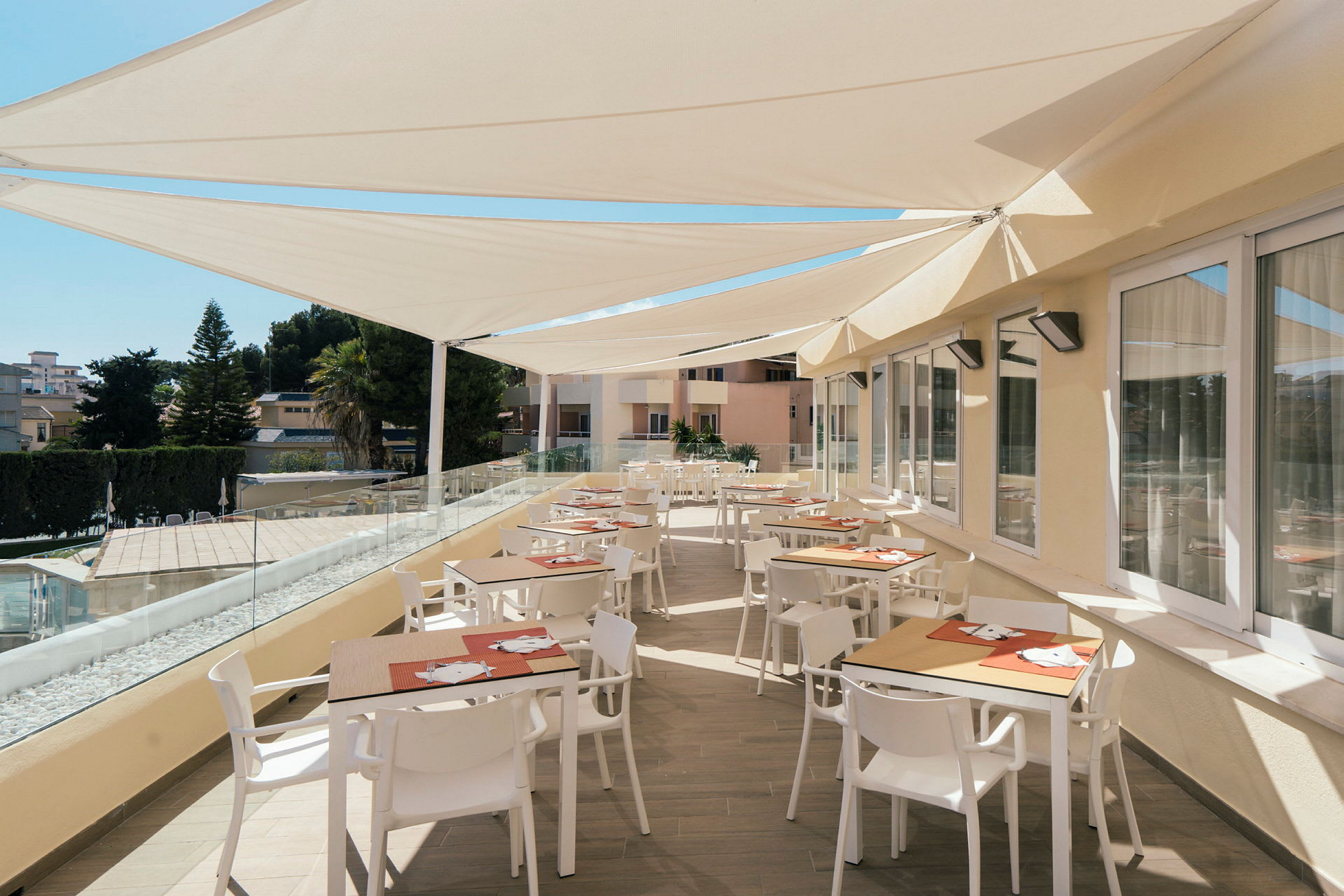 En terrasse med borde og stole under solafskærmning. (AI-genereret tekst)