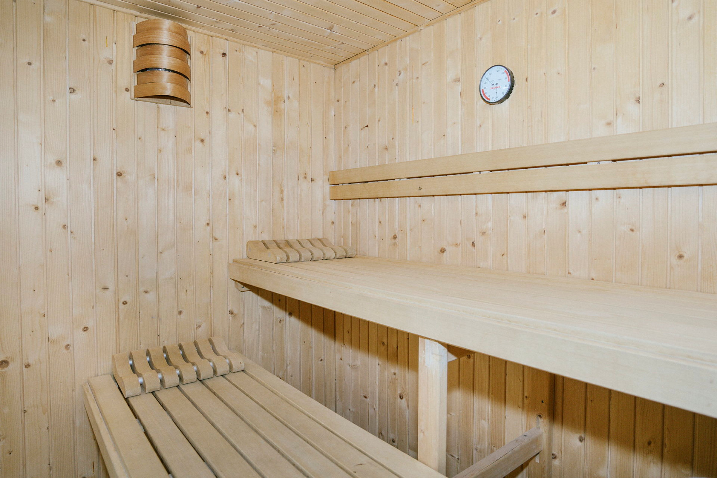 Billede af et træværelse i en sauna med bænke og et termometer på væggen. (AI-genereret tekst)