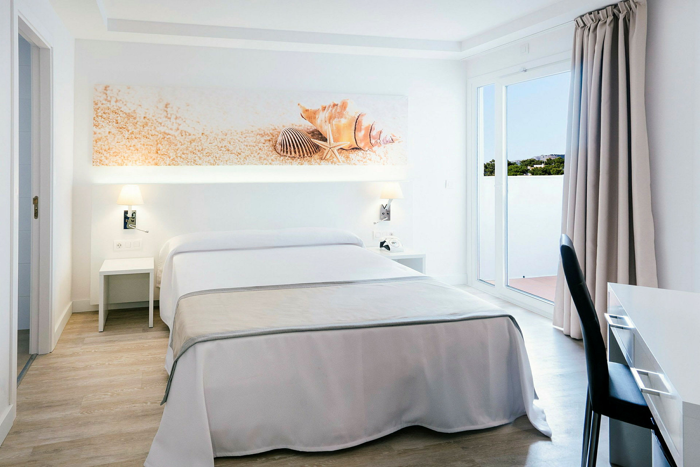 Et hotelværelse med dobbeltseng, hvid og beige indretning, dekoration med muslingeskaller over sengen. (AI-genereret tekst)