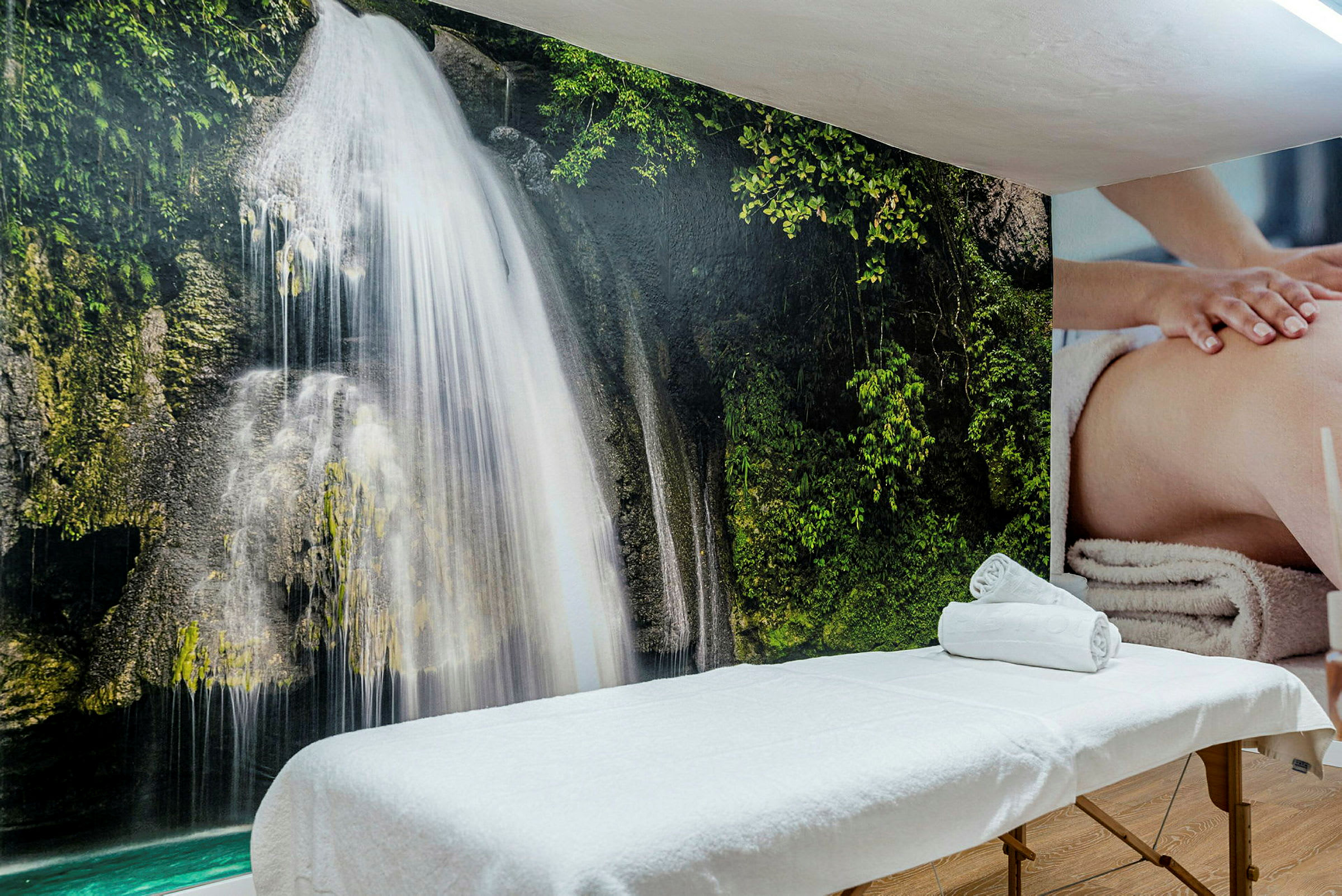 Massagebænk foran en væg med et billedmotiv af et vandfald. (AI-genereret tekst)