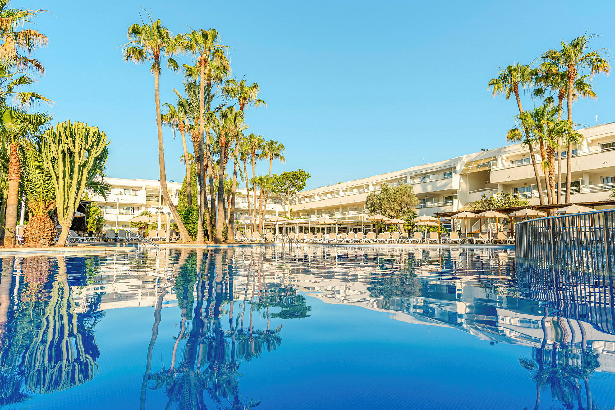 Billede af et hotel med palmer ved en pool. (AI-genereret tekst)