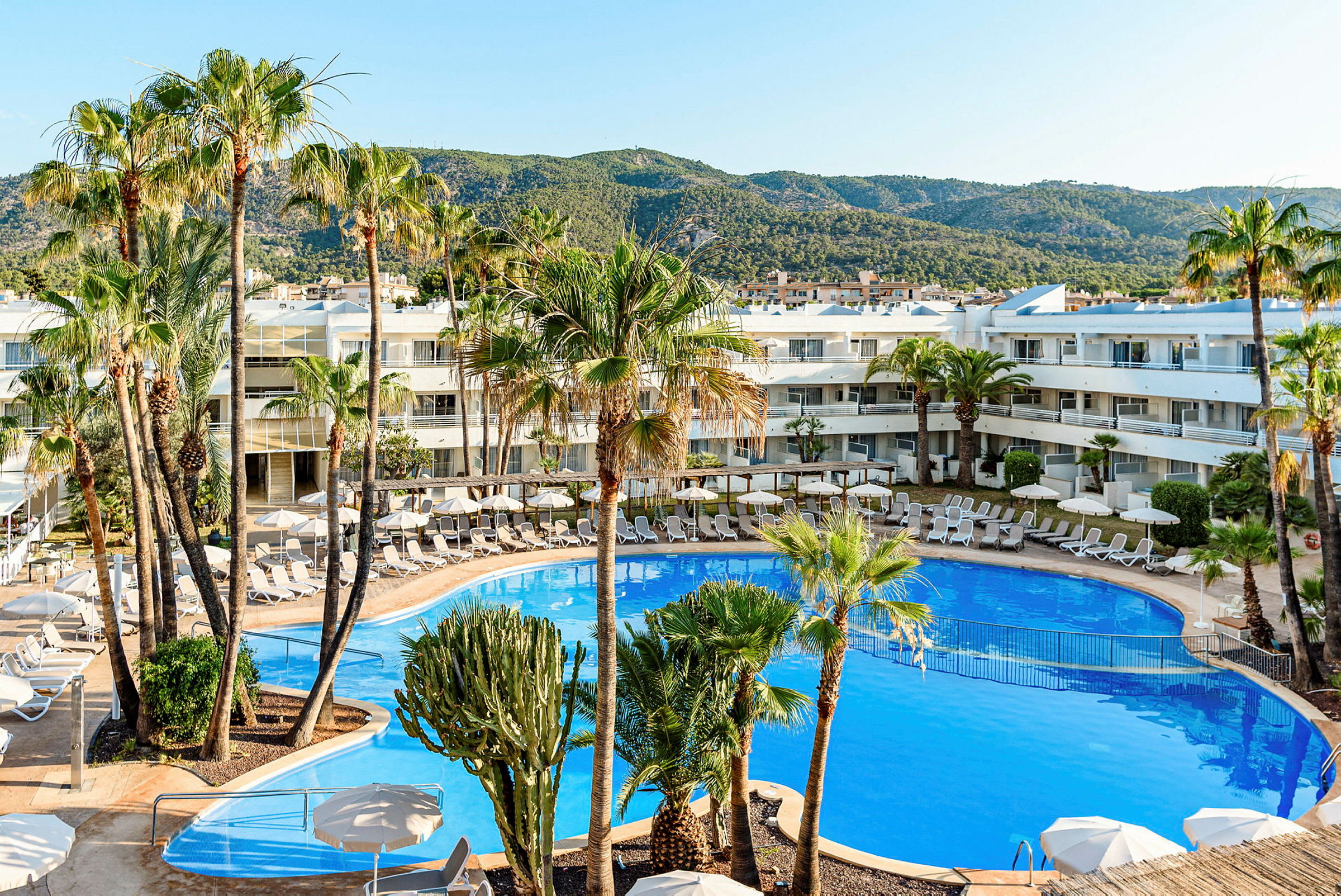 Poolområde ved hotel med omkringliggende palmer og liggestole. (AI-genereret tekst)