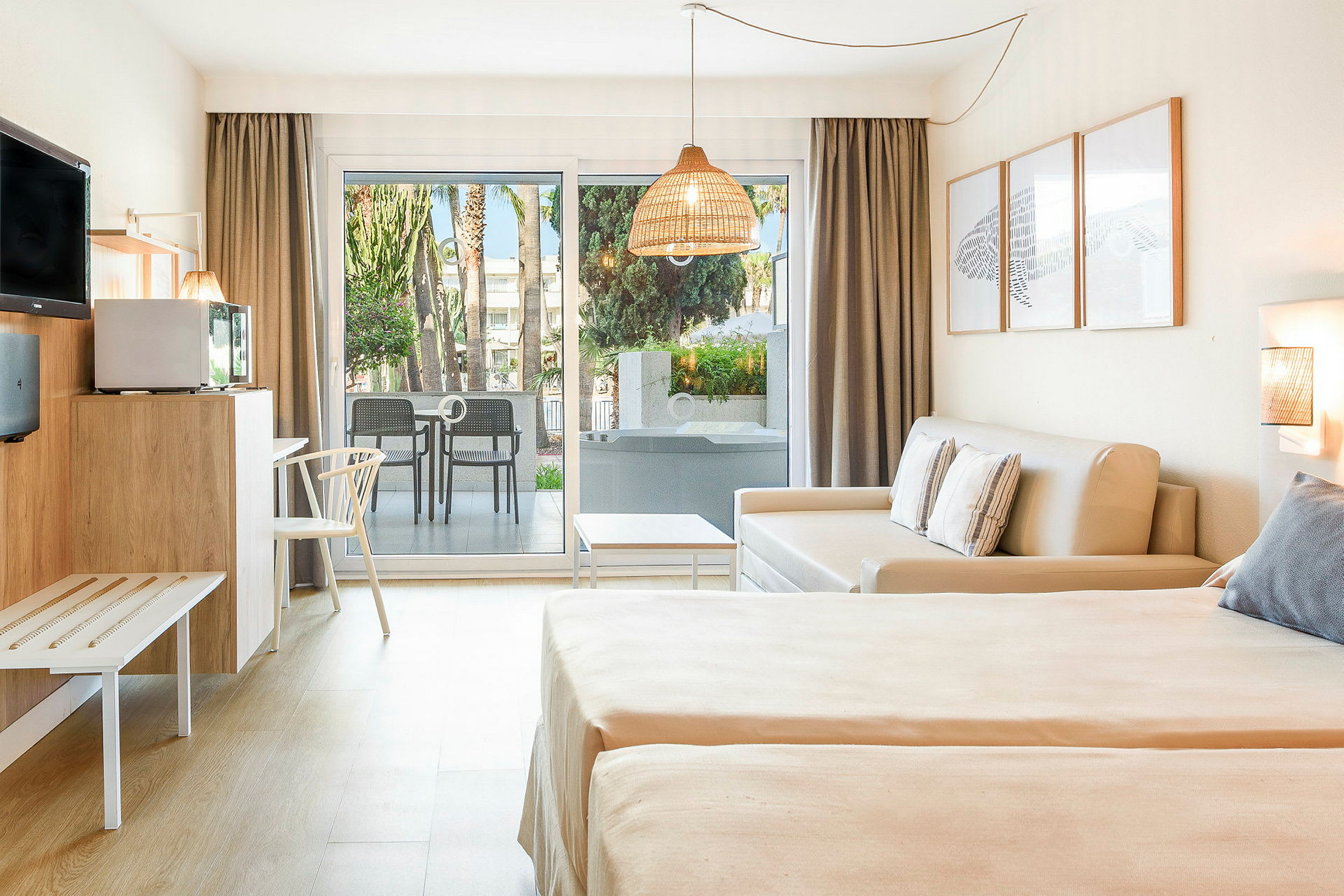 Et hotelværelse med lys indretning, en sovesofa, to senge og en terrasse med udsigt til grønne områder. (AI-genereret tekst)