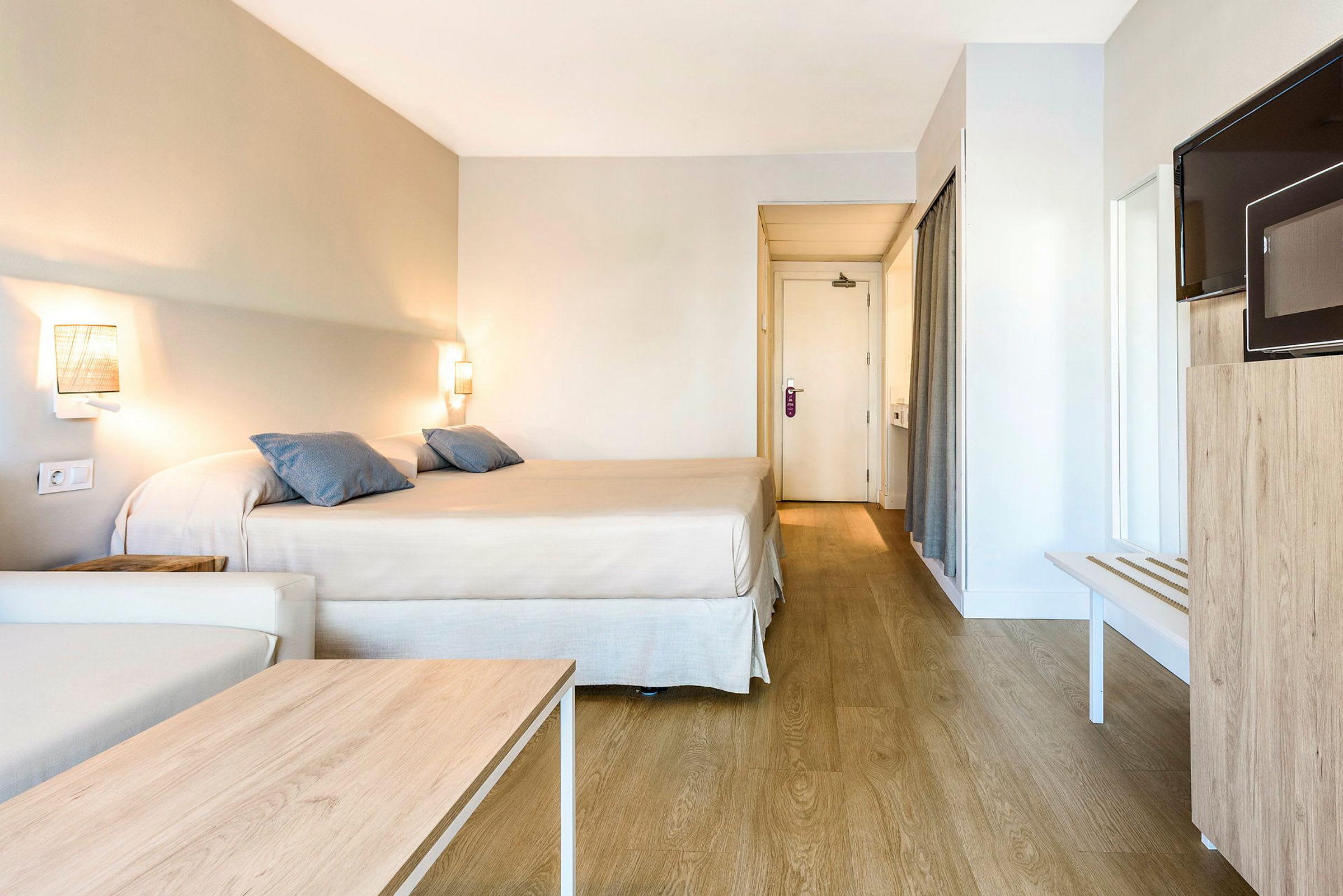 Hotelværelse med en dobbeltseng, en sofa, et træbord, et fjernsyn og en dør til badeværelset. (AI-genereret tekst)