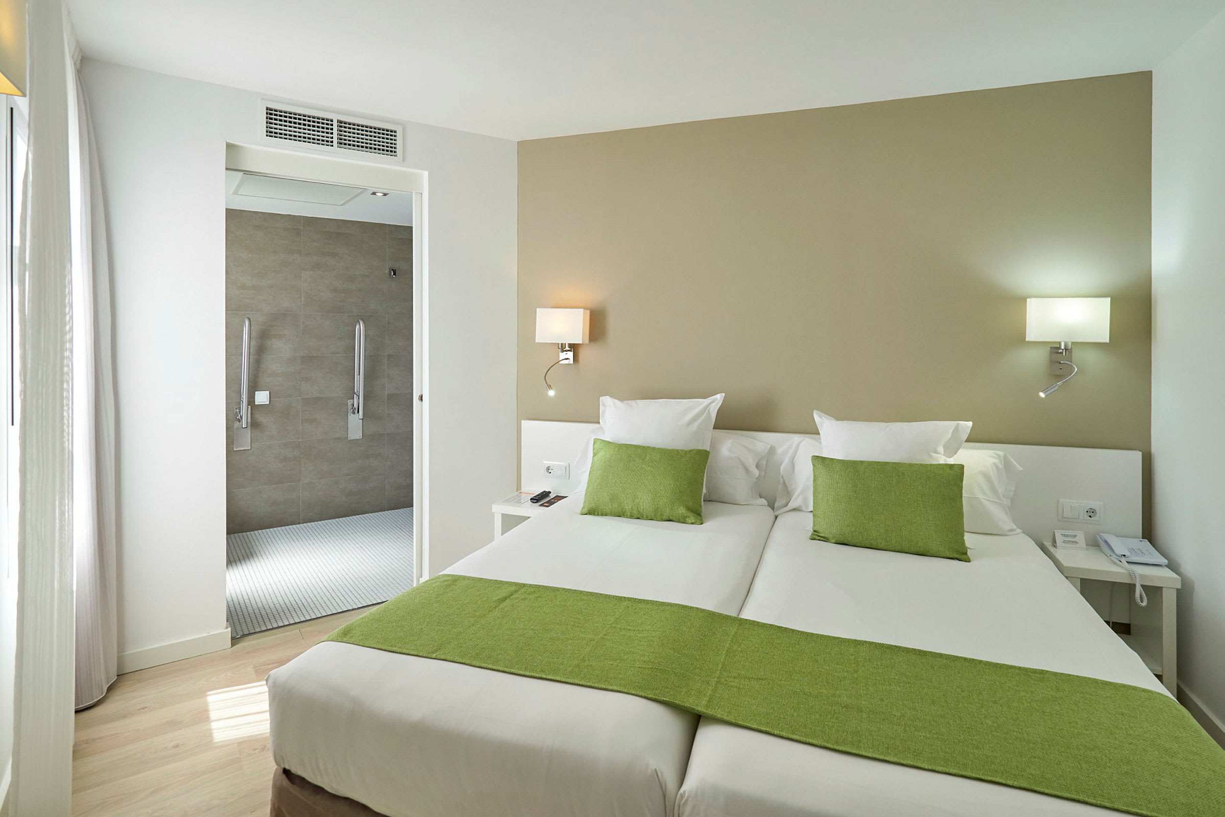 Hotelværelse med to enkeltsenge, grønt sengetøj og åbning til badeværelset. (AI-genereret tekst)