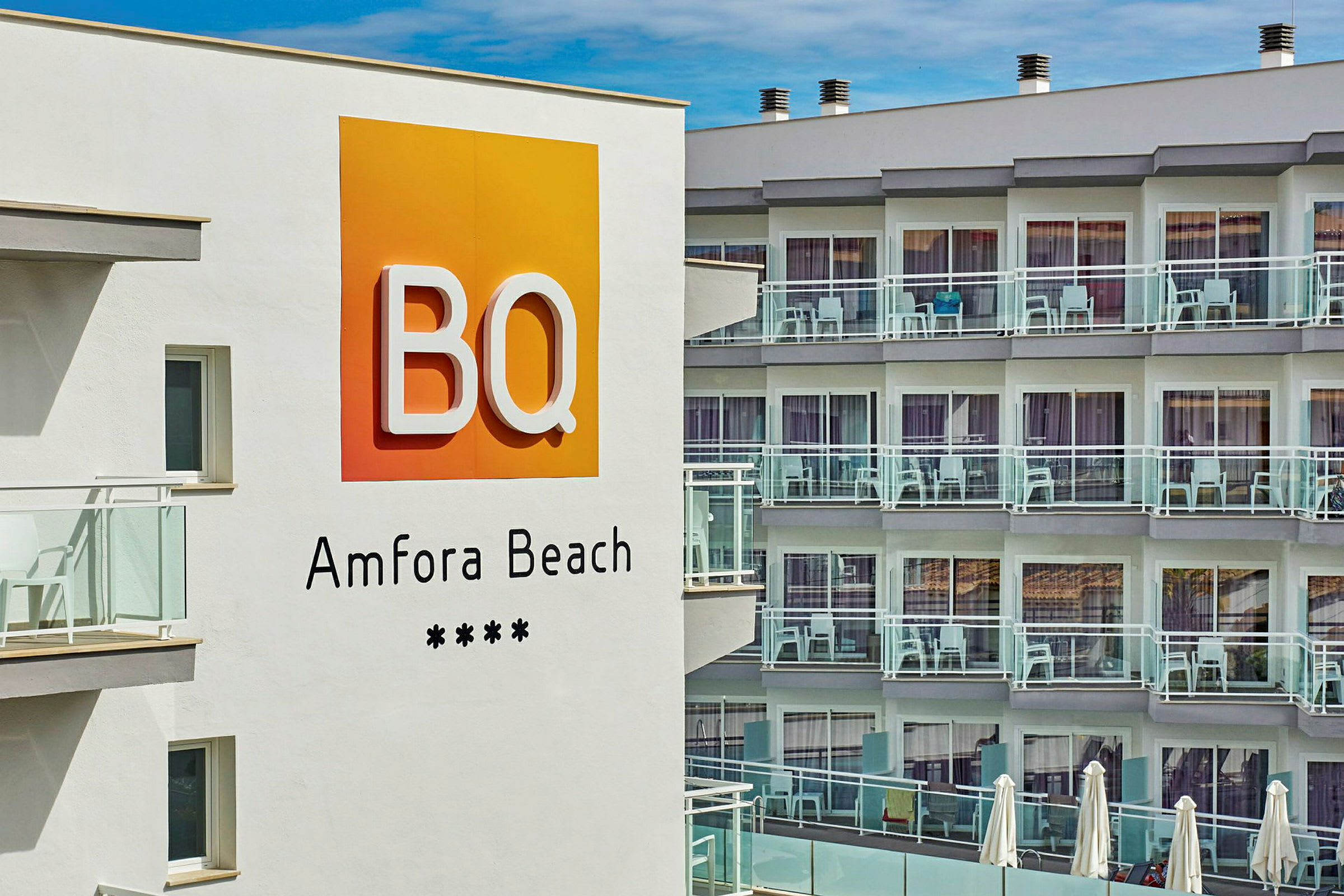Hotelskilt med teksten "BQ Amfora Beach" foran en bygning med altaner. (AI-genereret tekst)