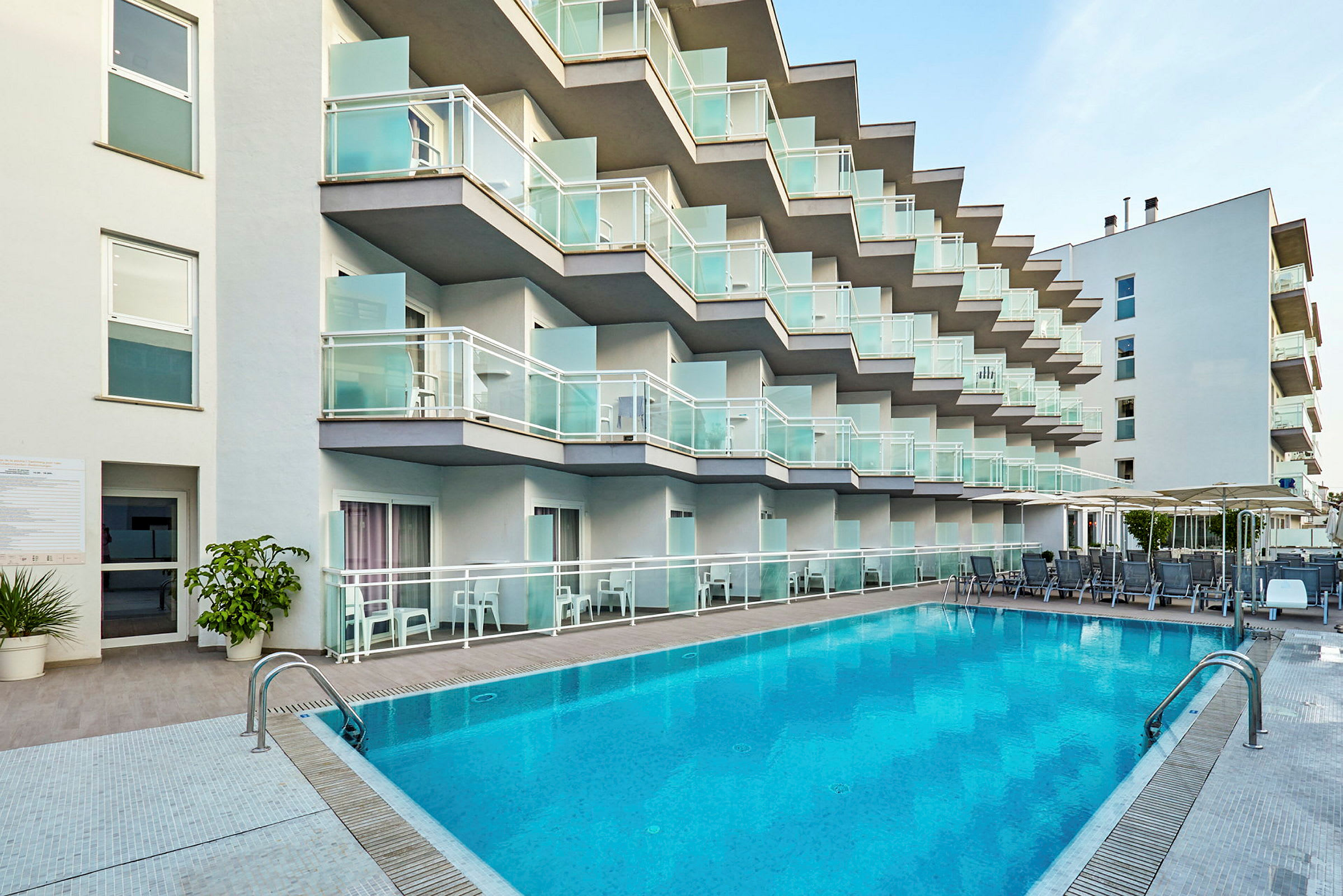 Hotelfacade med altaner og pool i forgrunden. (AI-genereret tekst)