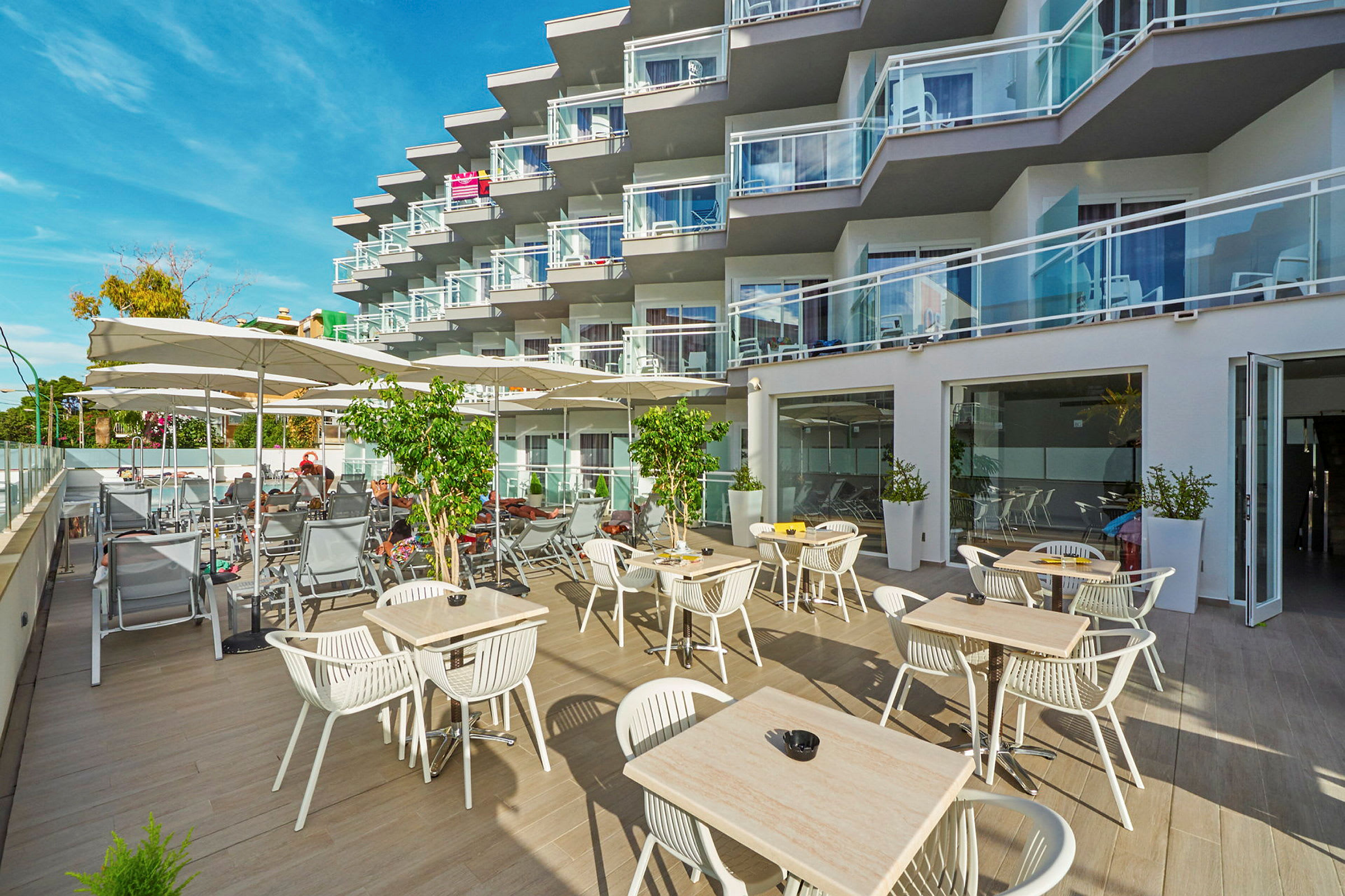 Udendørsområde med borde og stole samt liggestole ved et hotel med altaner. (AI-genereret tekst)