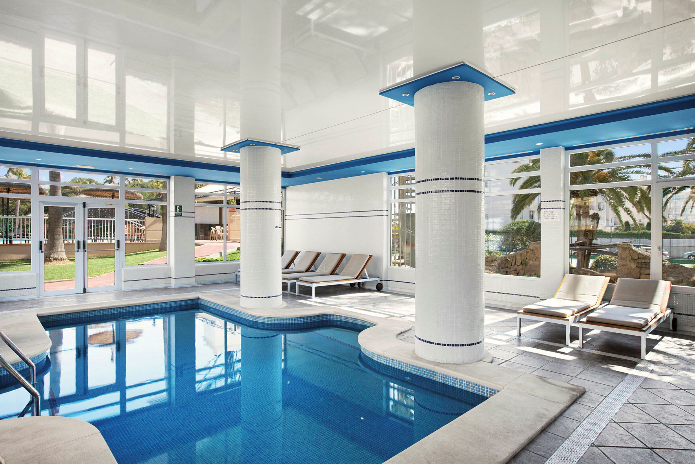 Indendørs pool med liggestole og store vinduer. (AI-genereret tekst)