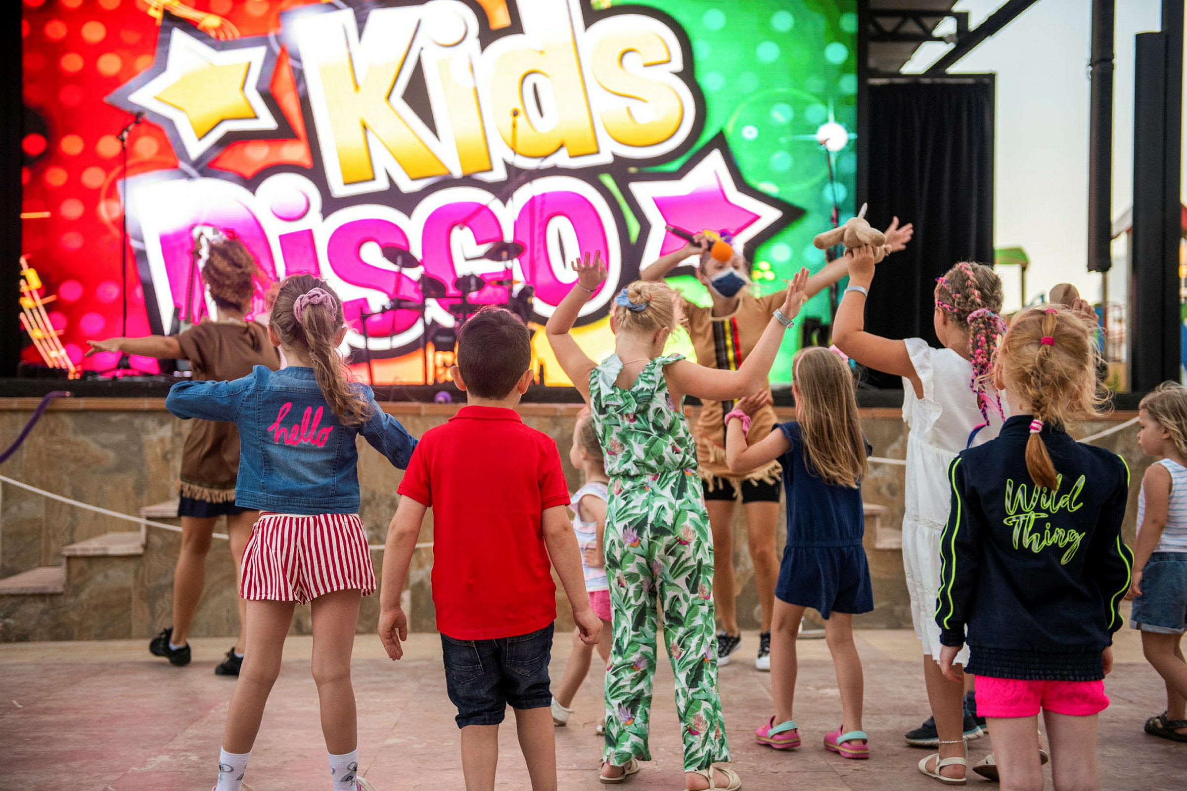 Børn, der danser foran et farverigt skilt med teksten 'Kids Disco'. (AI-genereret tekst)