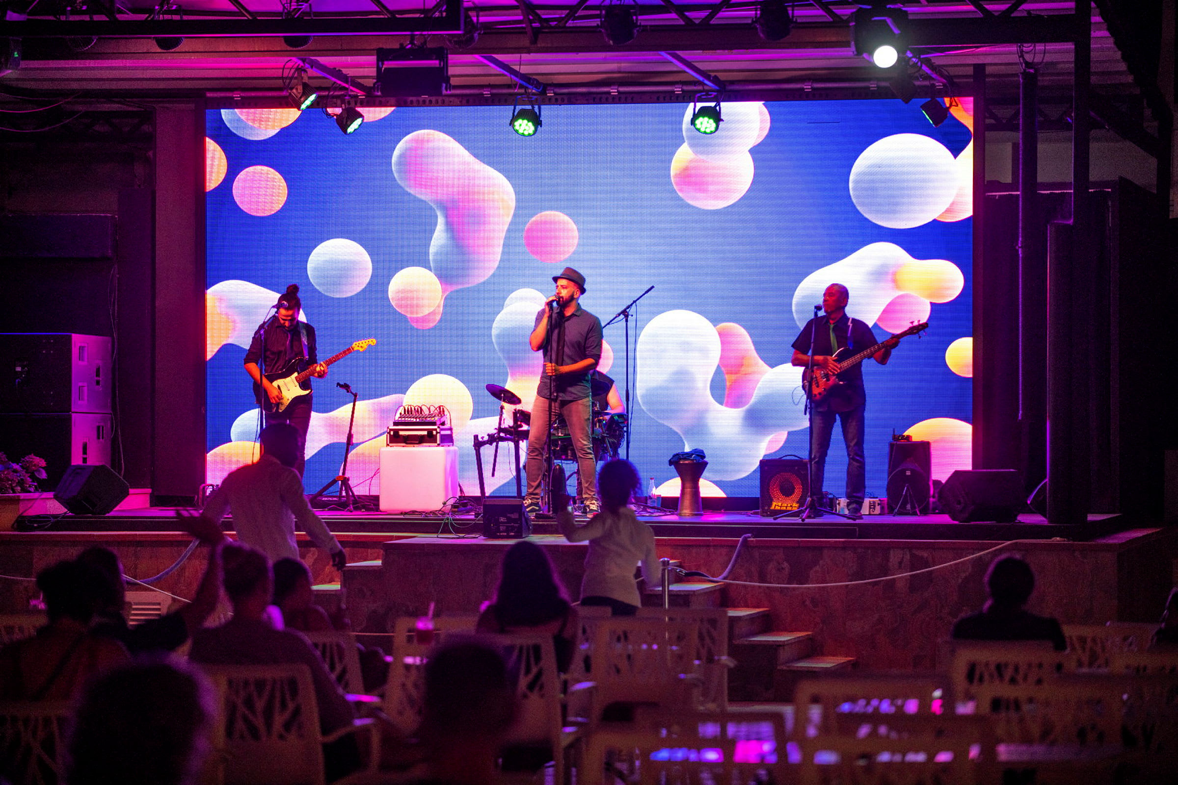 En musikkoncert med et band på scenen og en farverig baggrund. (AI-genereret tekst)