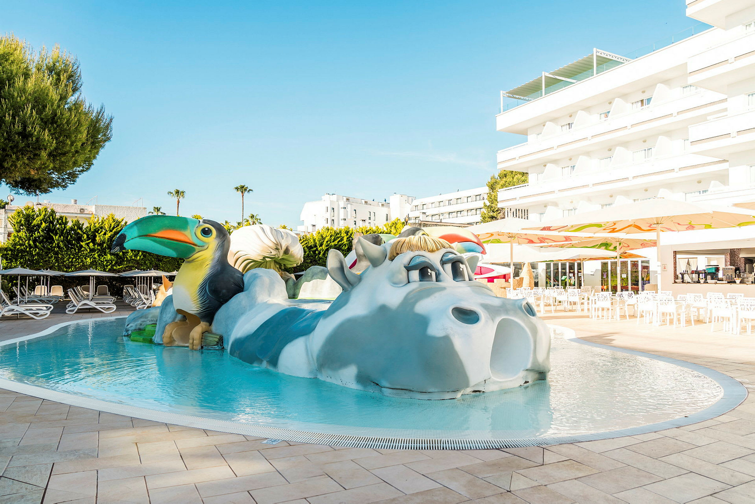 Pool med dekorativt dyremotiv, omgivet af liggestole og bygninger. (AI-genereret tekst)