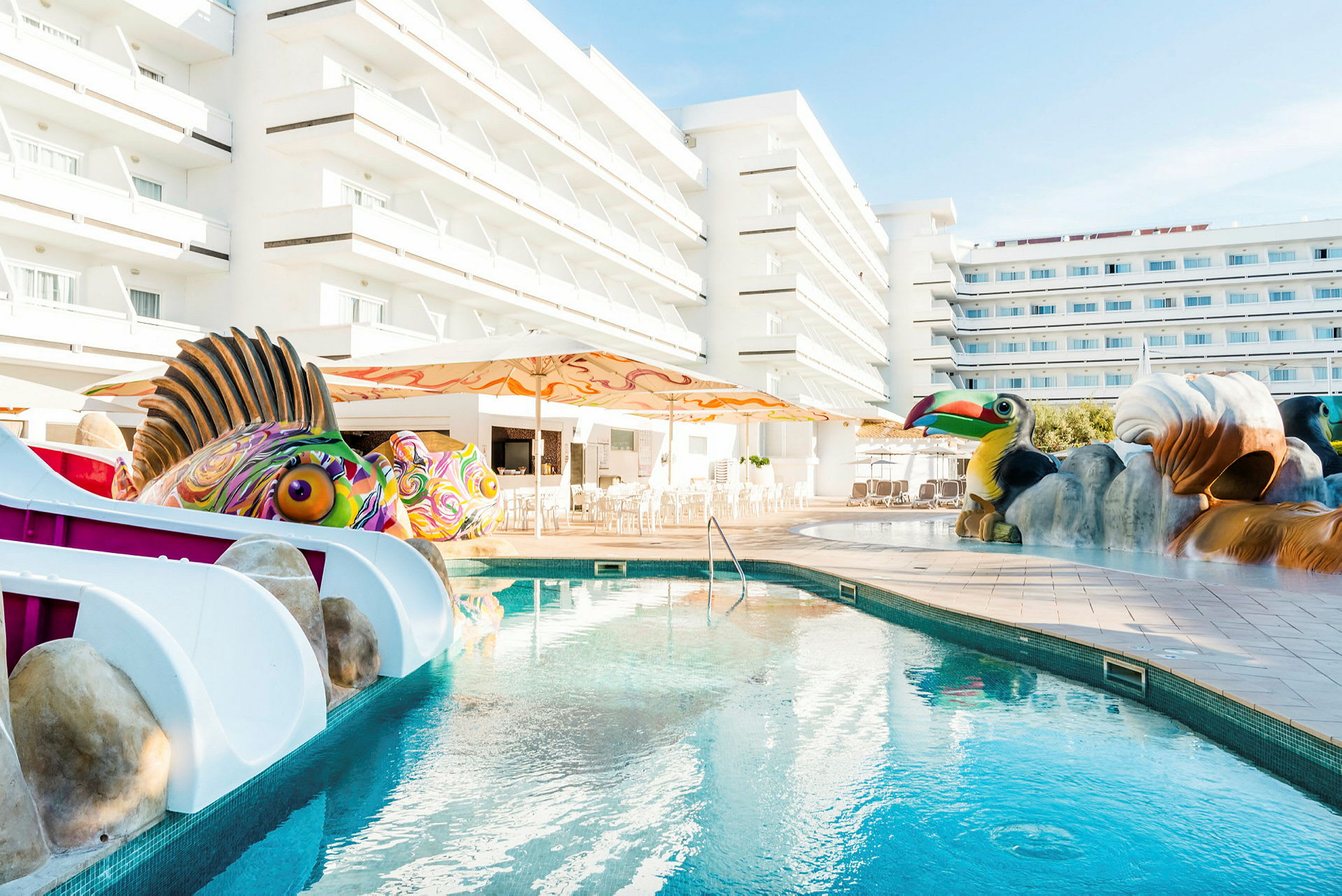 En pool med legetøjs-havdyr og dyrefigurer foran hotelbygninger. (AI-genereret tekst)