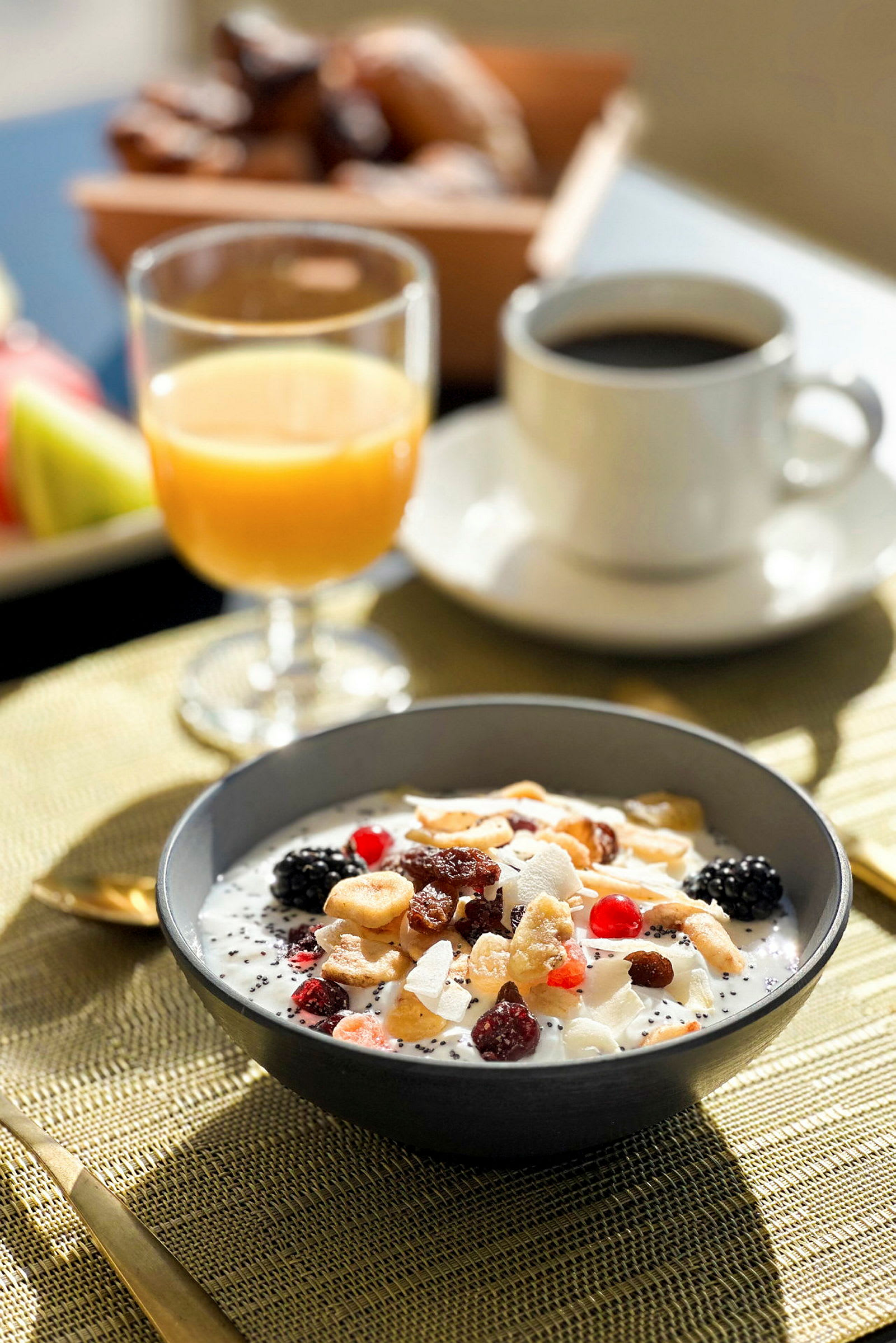 En morgenmadsskål med yoghurt, frugt og nødder ved siden af et glas appelsinjuice og en kop kaffe. (AI-genereret tekst)