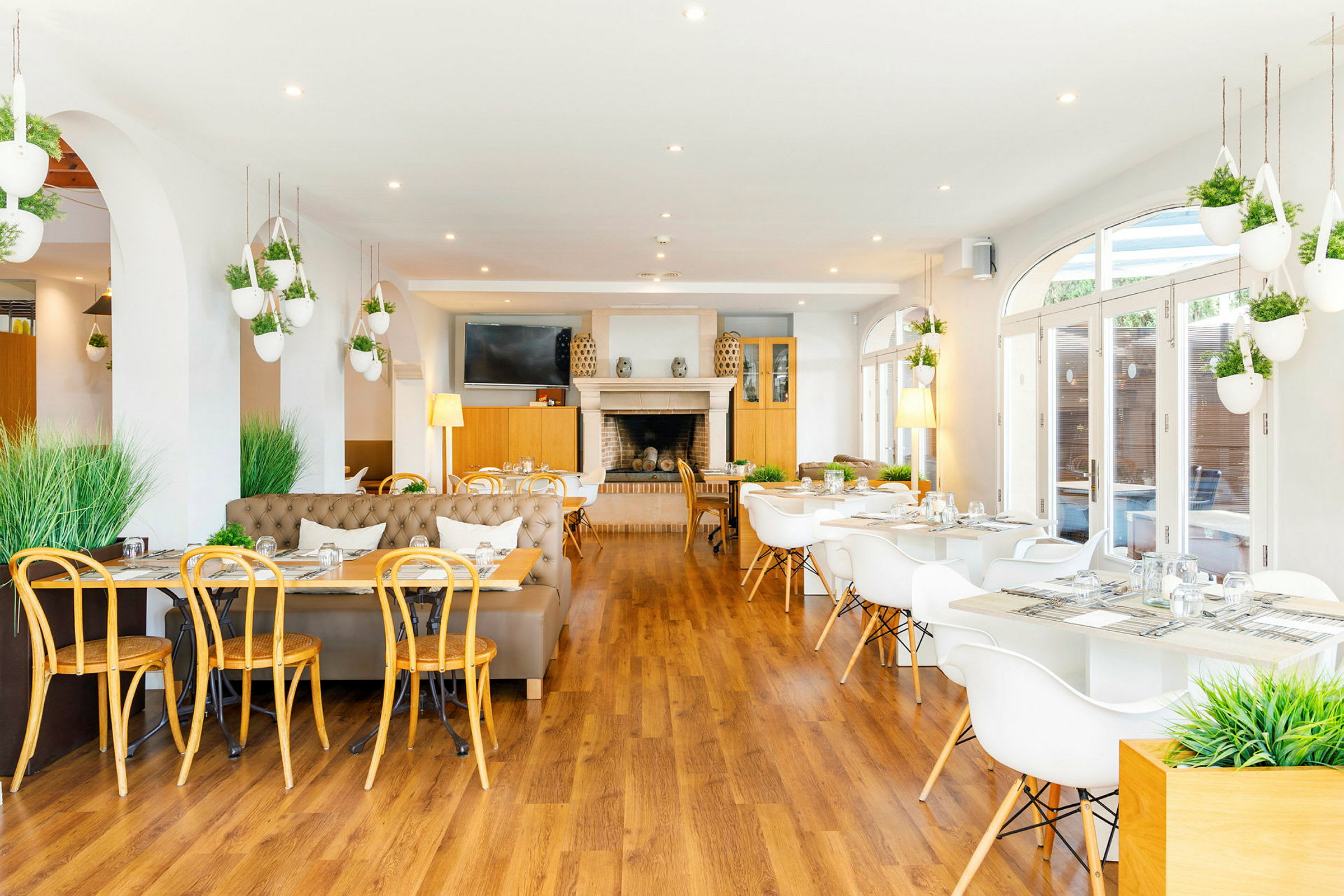 En lys restaurant med moderne møbler og hvide borde omgivet af grønne planter. (AI-genereret tekst)