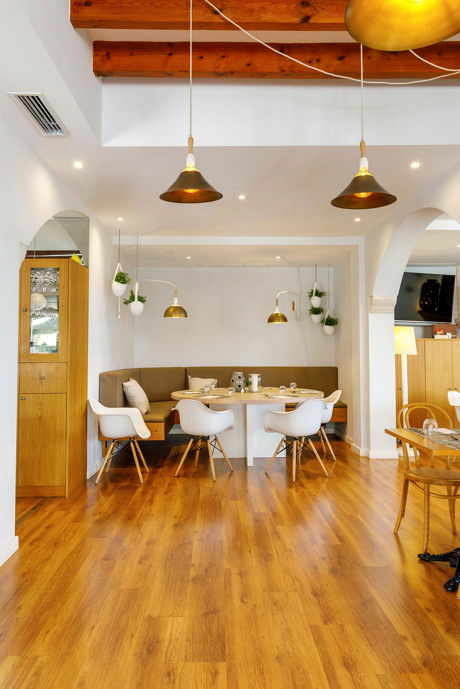 Et moderne restaurantinteriør med trægulv, et bord med stole og sofaer, og hængende lamper. (AI-genereret tekst)