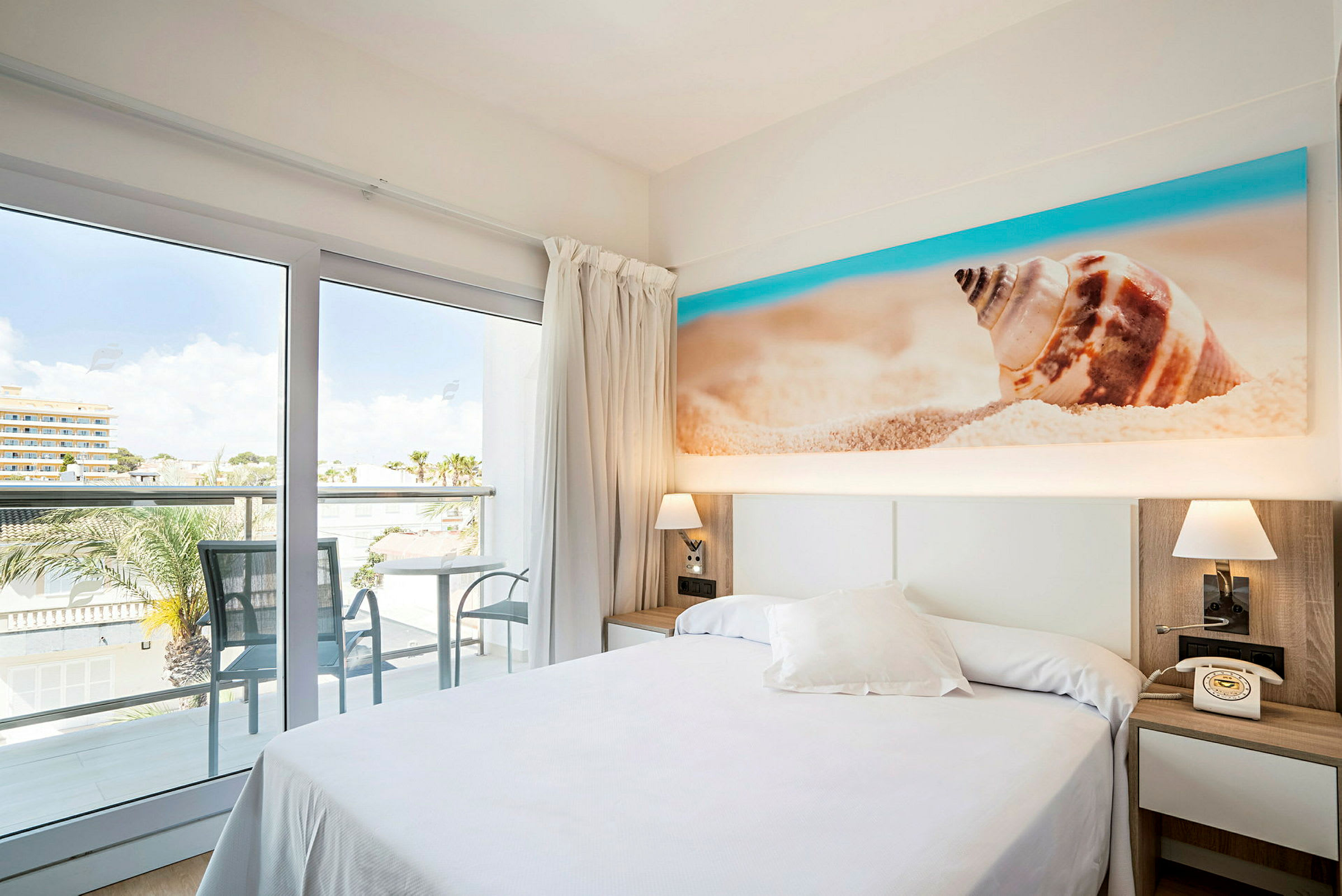 Hotelværelse med balkon og udsigt, seng og dekoration med strandmotiv. (AI-genereret tekst)