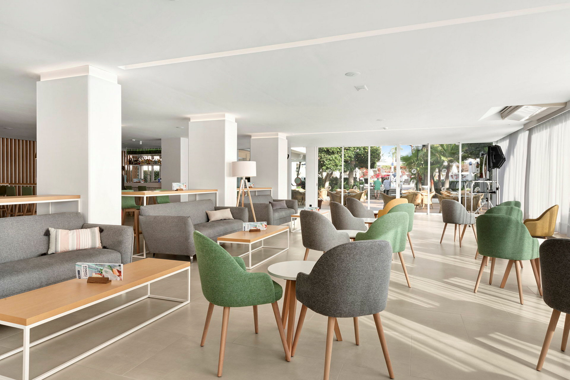 En lys og moderne lounge med grønne og grå stole, borde og store vinduer. (AI-genereret tekst)