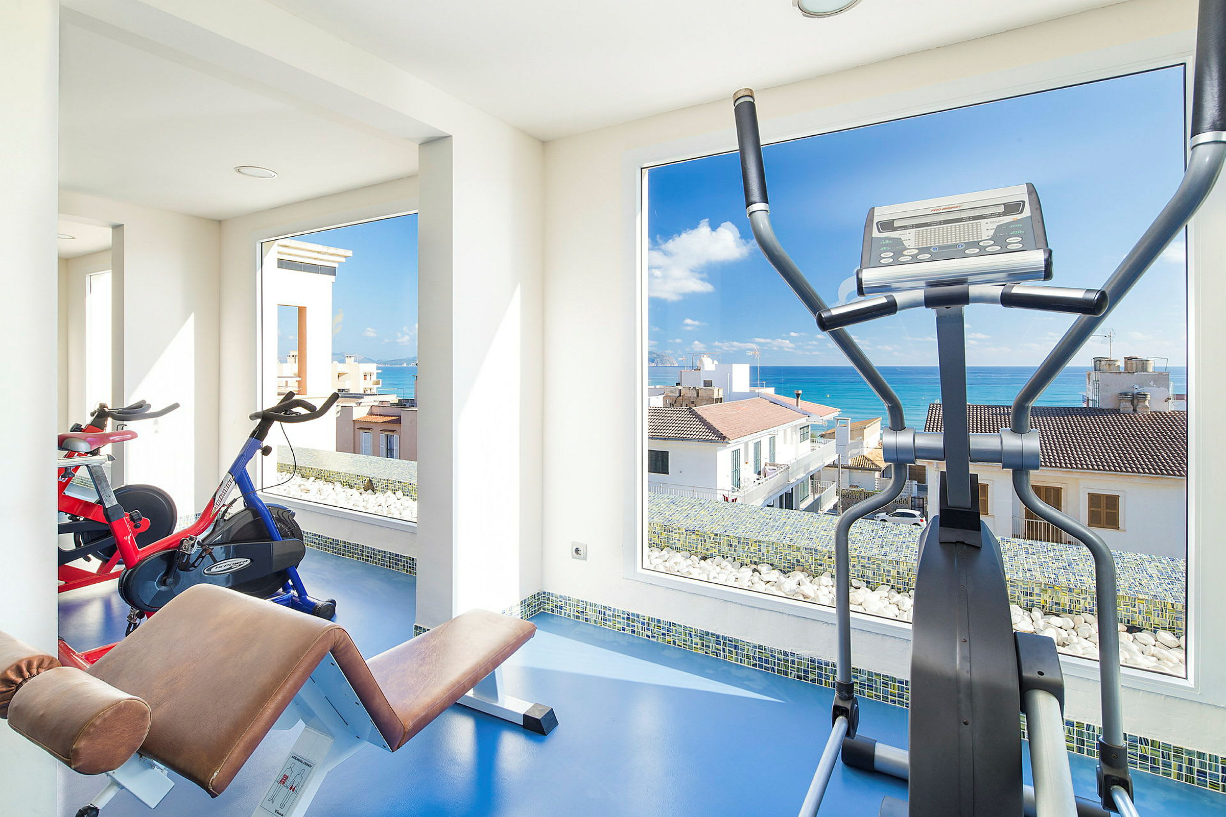 Et træningsrum med fitnessudstyr og udsigt over havet. (AI-genereret tekst)