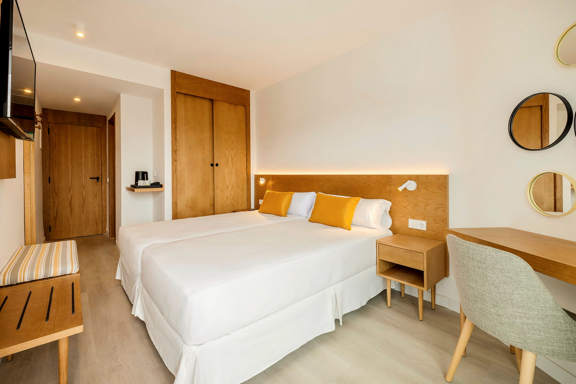 Et lyst og moderne indrettet hotelværelse med to enkeltsenge, trømøbler og gulddetaljer i tekstiler. (AI-genereret tekst)